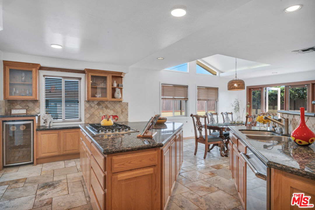Kitchen with a granite island and gas cooktop, wood cabinetry, and an adjoining dining area.