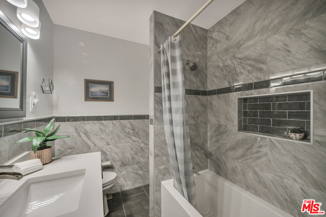 Bathroom with gray marble-look tile, a dark tiled shower niche, and a striped curtain.