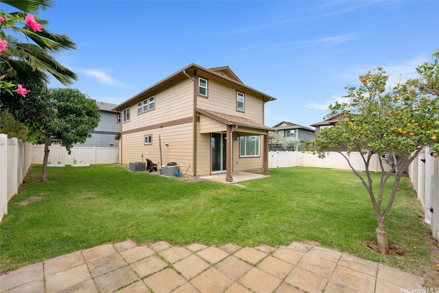 Two-story beige home behind a fenced lawn, with a covered patio and citrus trees.