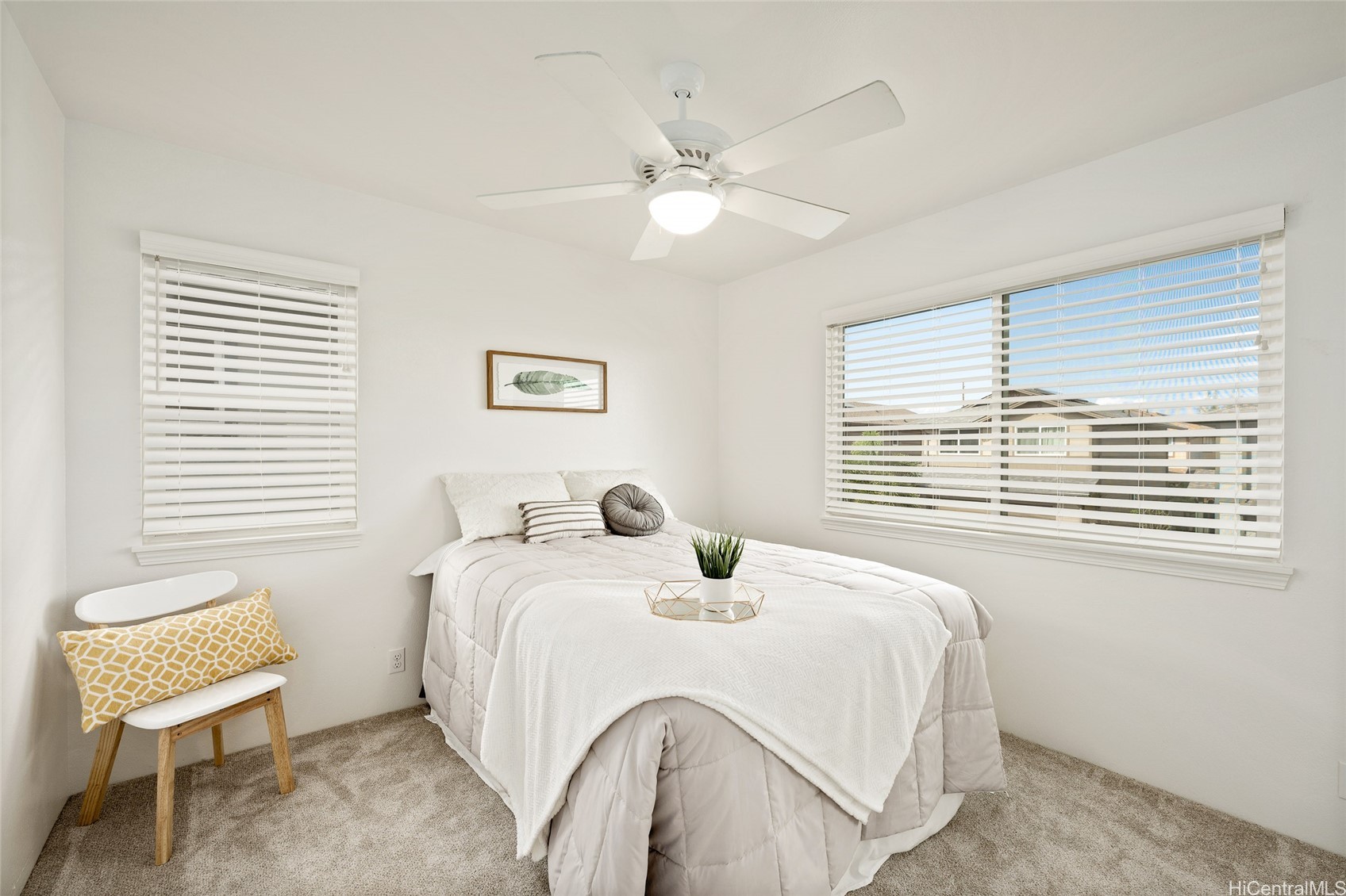 Staged bedroom with a white bed, ceiling fan, and wide windows with blinds.
