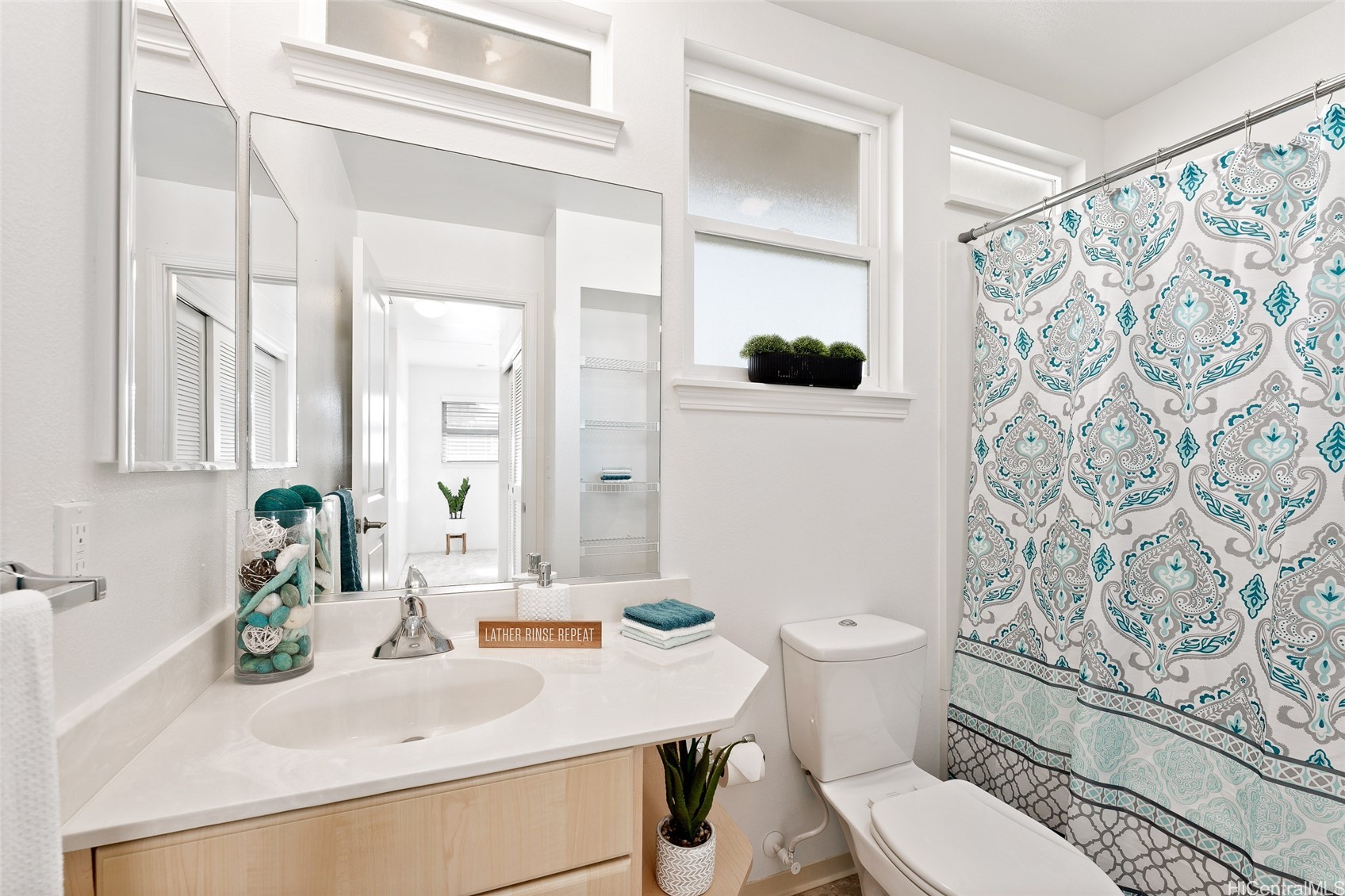 Bright bathroom with a light wood vanity, large mirror, and teal patterned shower curtain.