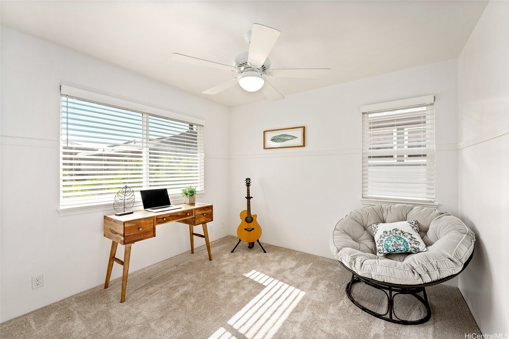 Bright home office with a wooden desk, guitar, and round cushioned chair.