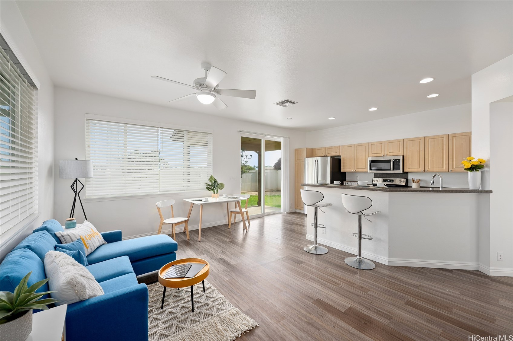 Open-plan living room and kitchen with a blue sectional, wood cabinets, and sliding doors to the yard.