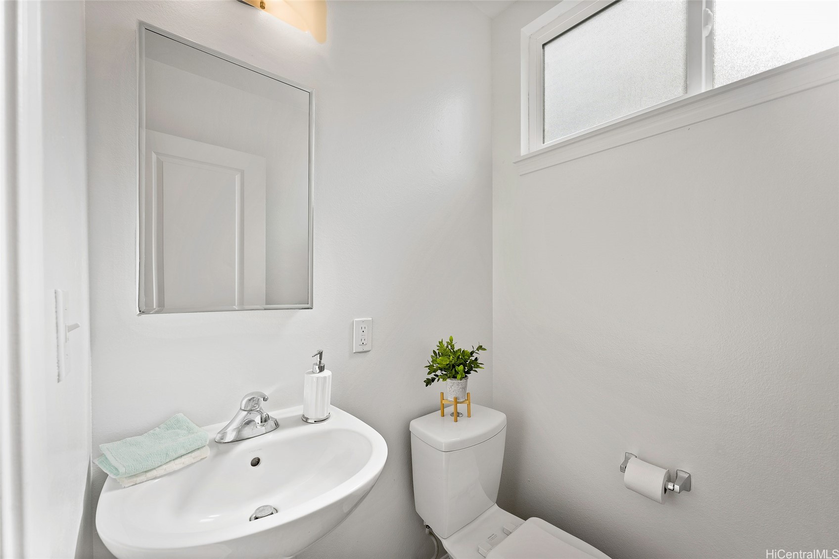 Bright bathroom with a white sink, large mirror, toilet, and frosted window.