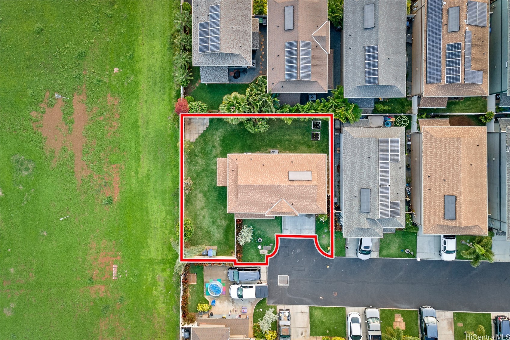 Aerial view of a home and yard outlined in red, beside a large grassy area.