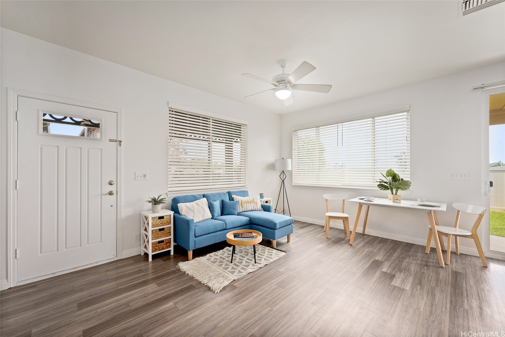 Living and dining room with a blue sectional, white dining set, and wide windows with blinds.