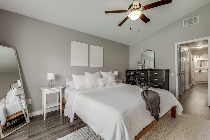 Bedroom with a white bed, dark dresser, ceiling fan, and adjoining bathroom doorway.