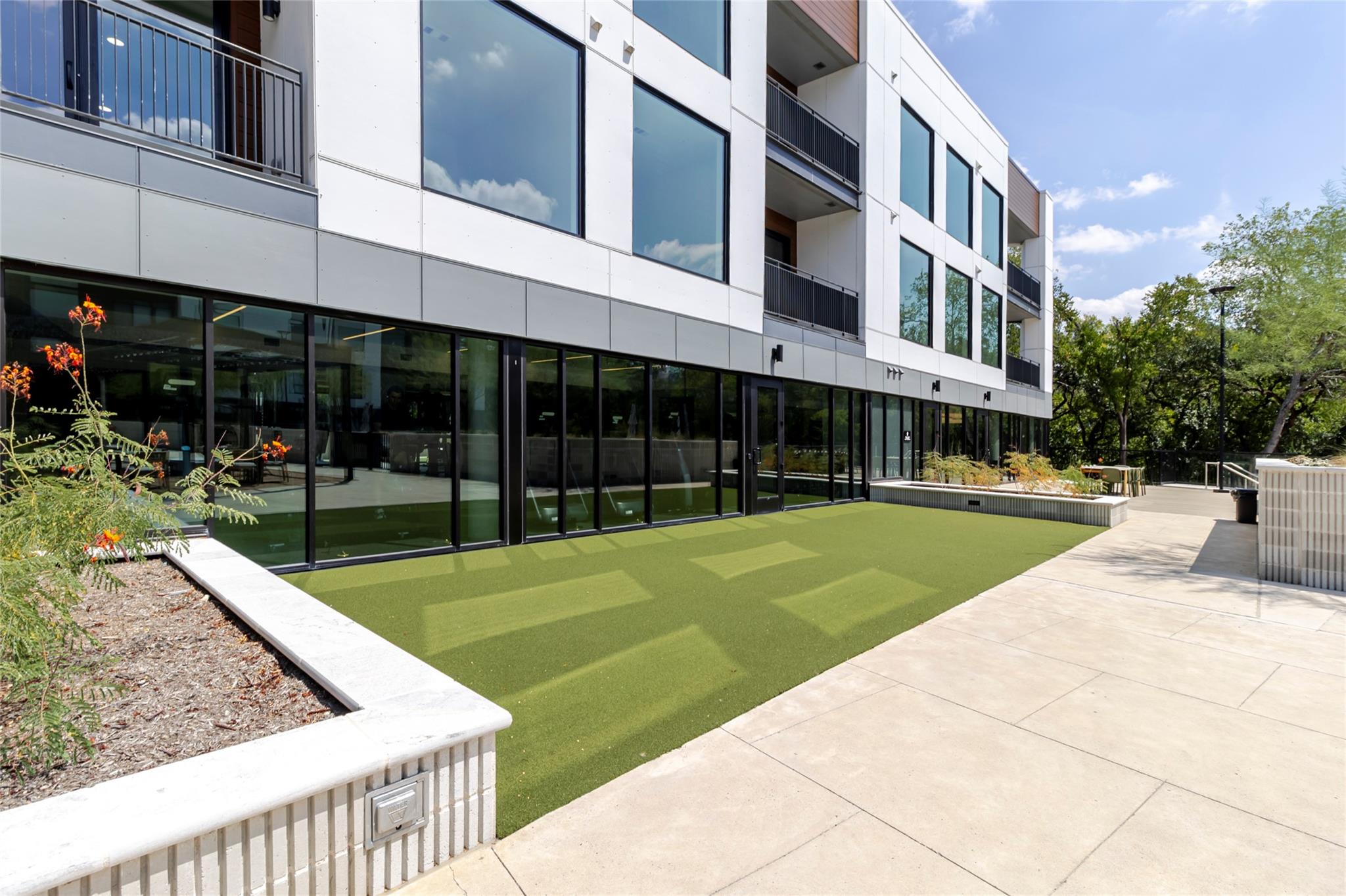 Modern condominium courtyard with artificial turf, concrete walkways, raised planters, and outdoor seating.