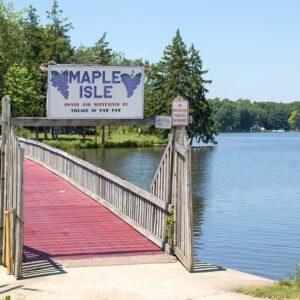 Red-planked ramp with wooden railings extends over a lake beside a Maple Isle sign.