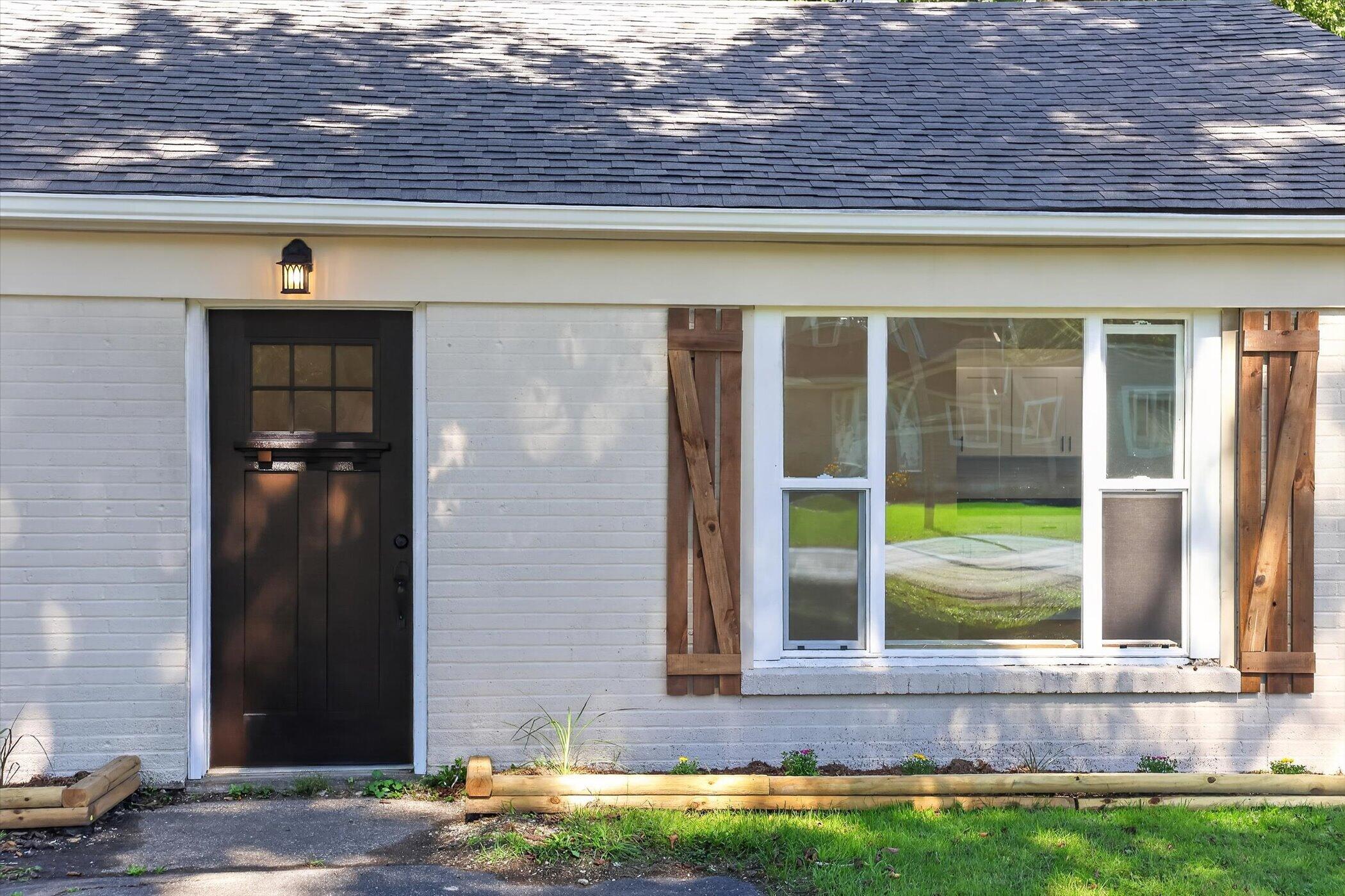 Home exterior with a dark entry door and a large window framed by rustic wooden shutters.