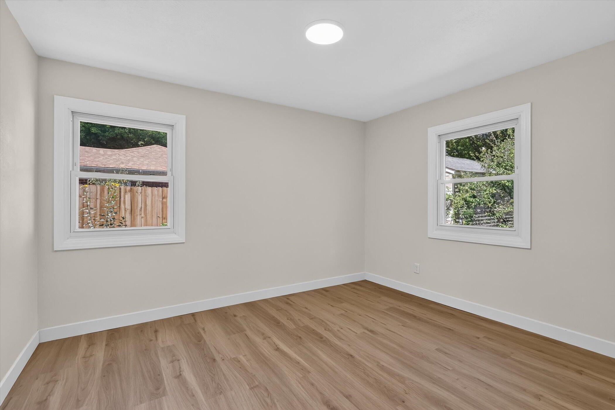 Empty room with light wood-look flooring, two windows, and a round ceiling light.