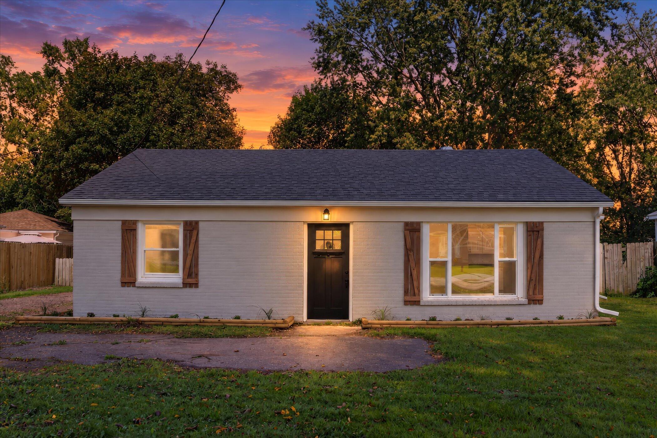 Single-story brick house with wood shutters and a lit front door at dusk.