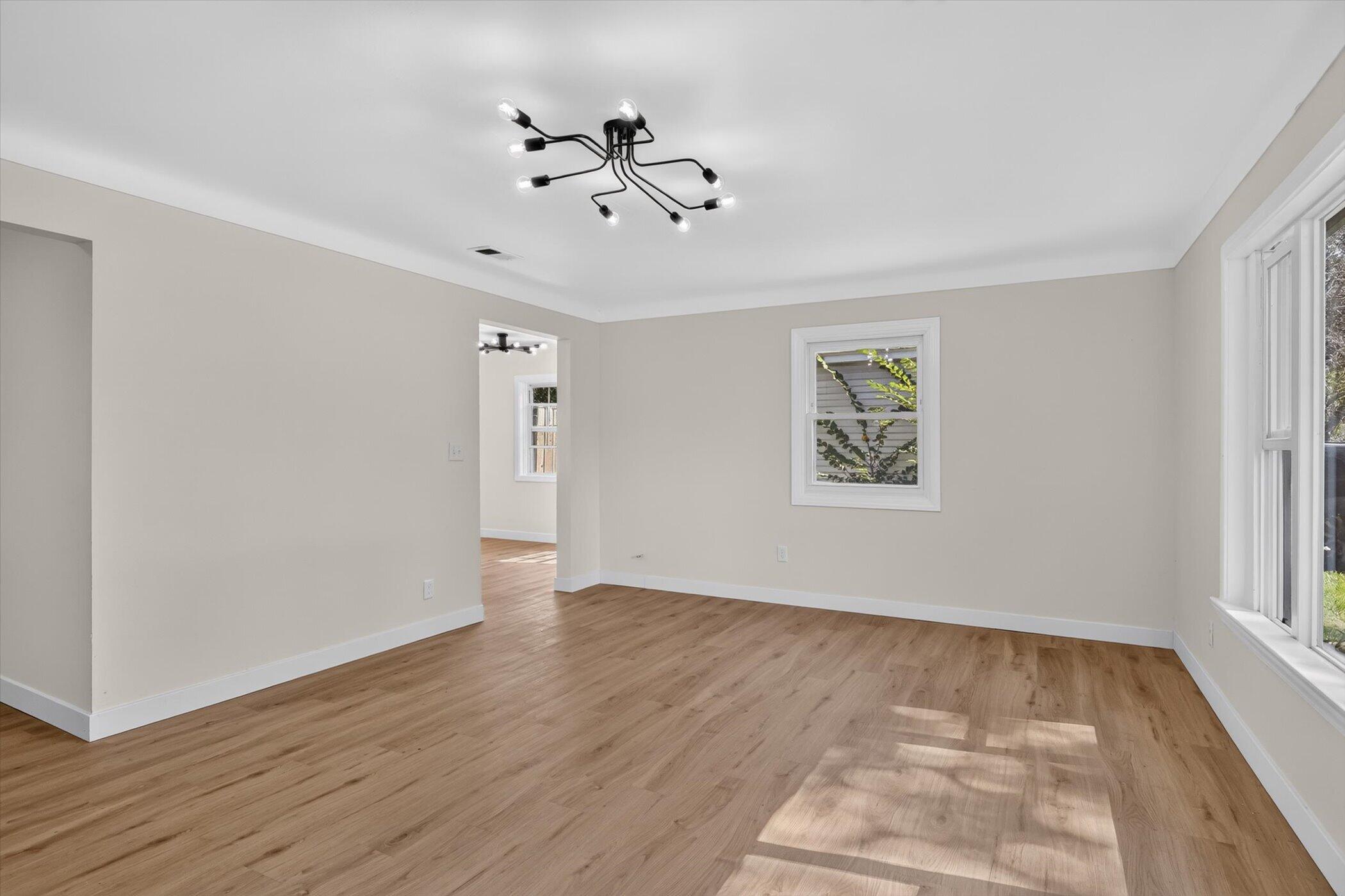 Empty room with light wood floors, a branching ceiling light, and sunlight through tall windows.