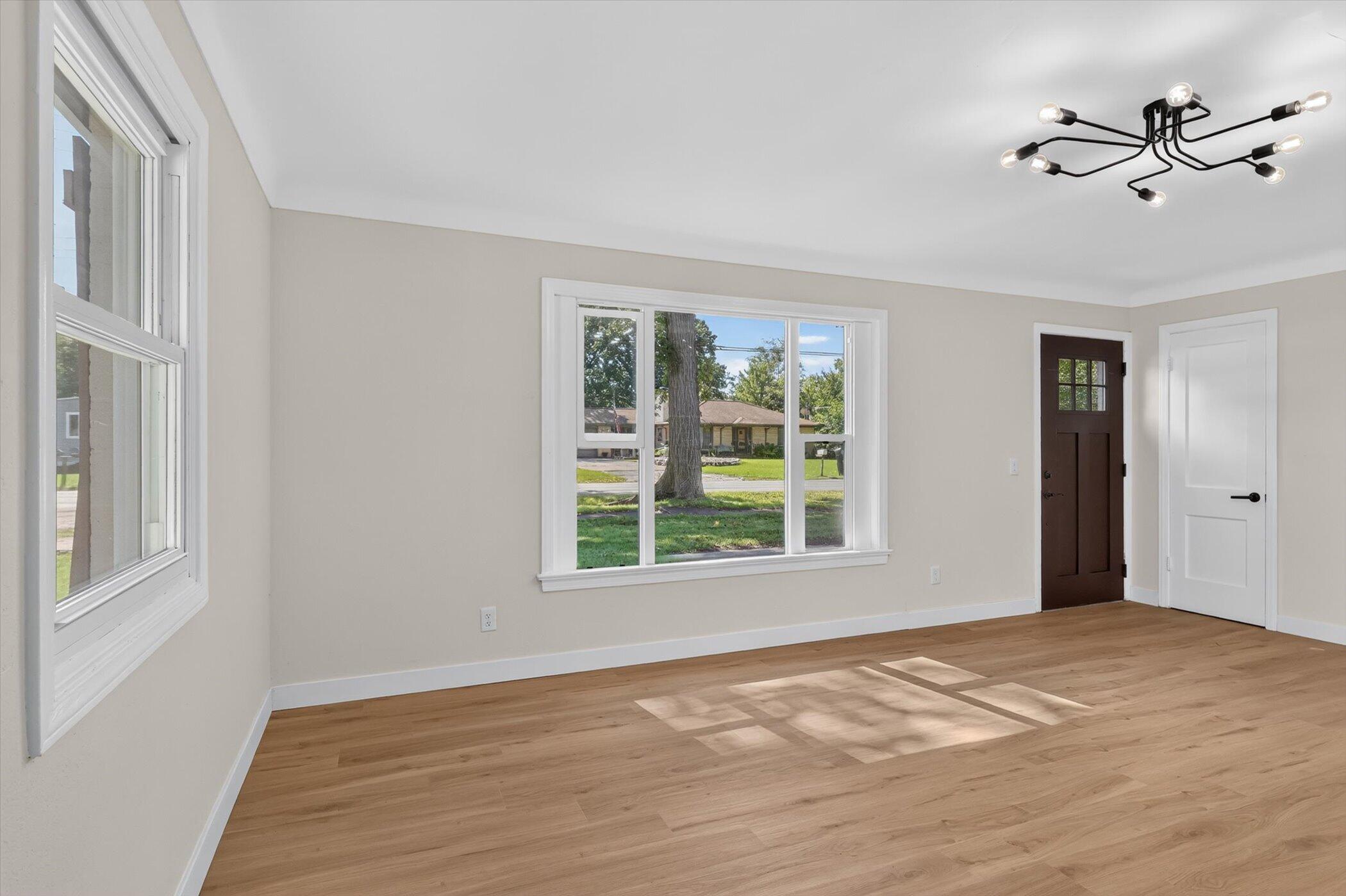 Empty room with light wood floors, large windows, and a modern chandelier.