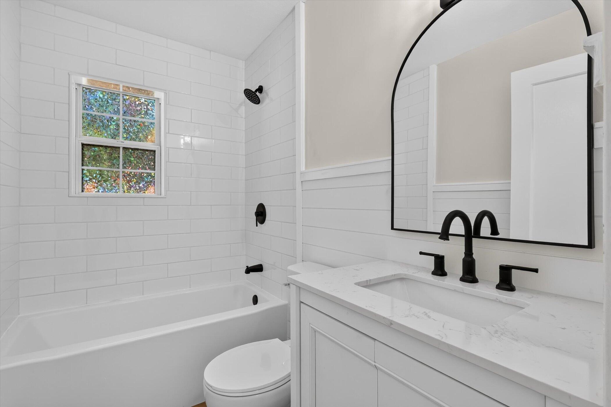 Bathroom with a white subway-tile tub surround, black fixtures, and a vanity beneath an arched mirror.