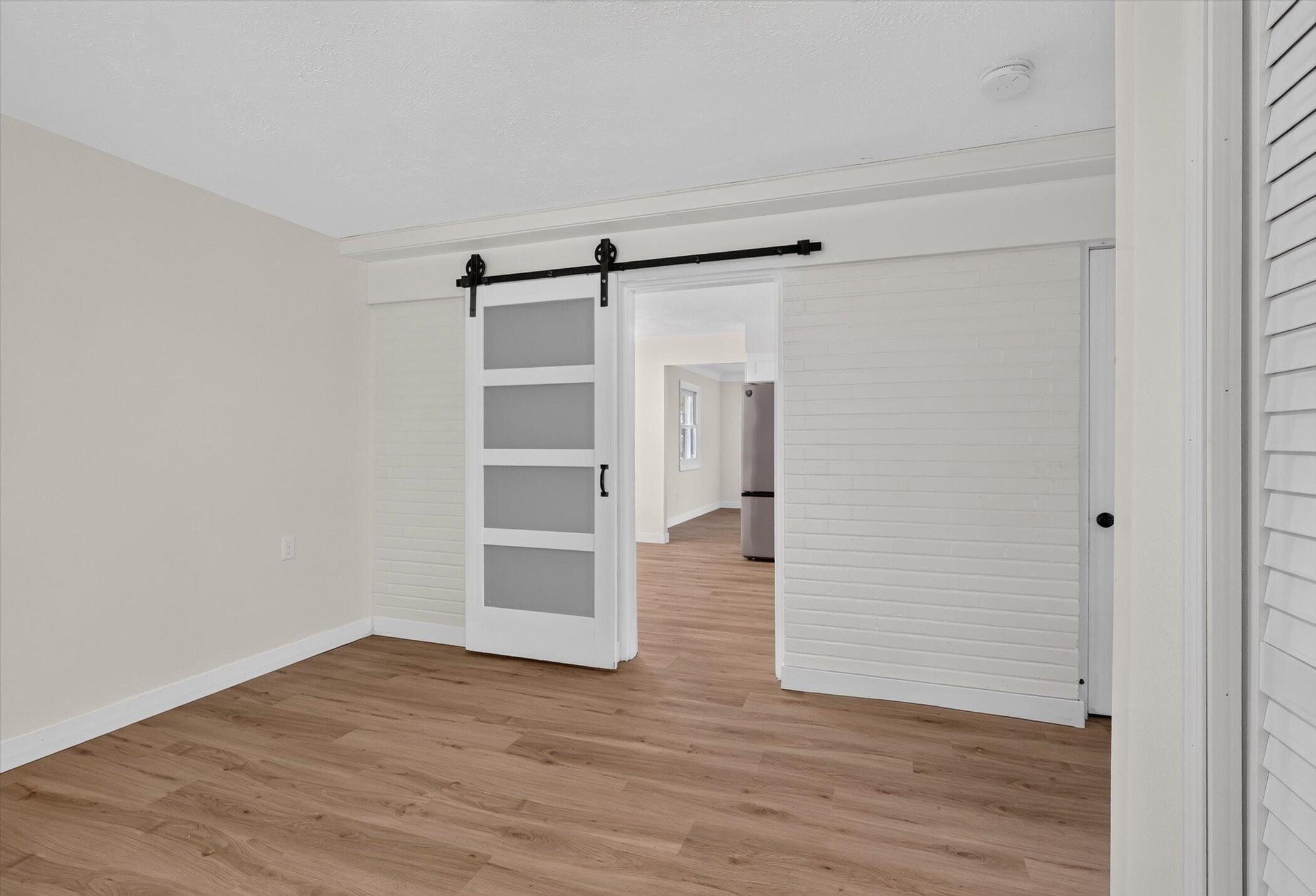 Empty room with wood-look floors and a white sliding barn door with gray panels.
