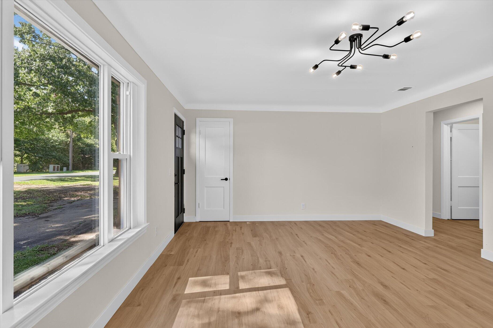 Vacant living room with wood floors, large windows, and a modern branching ceiling light.