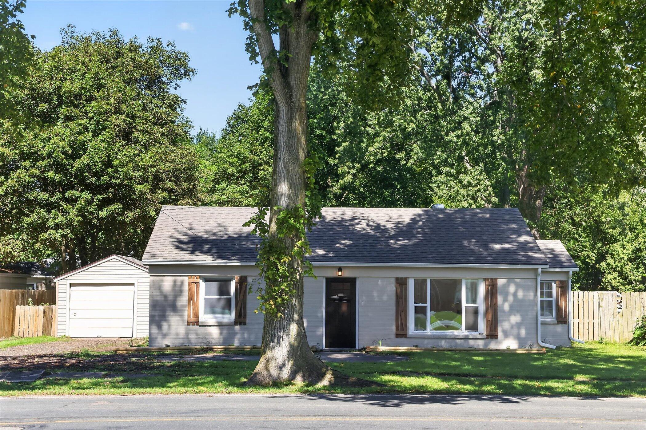 Gray single-story house with wood shutters and a large tree partly obscuring the front facade.