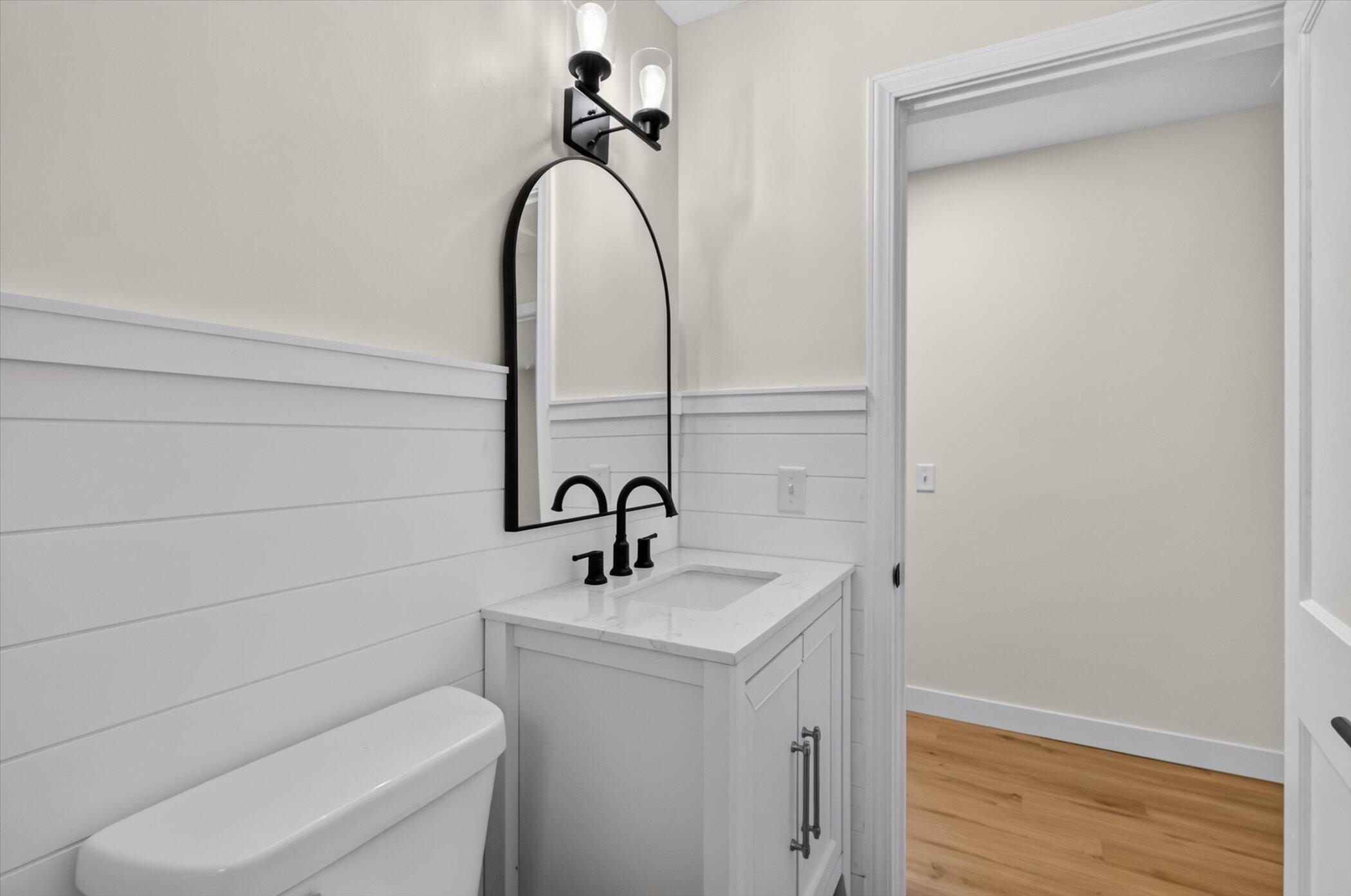Bright bathroom with white shiplap, a white vanity, black fixtures, and an arched mirror.