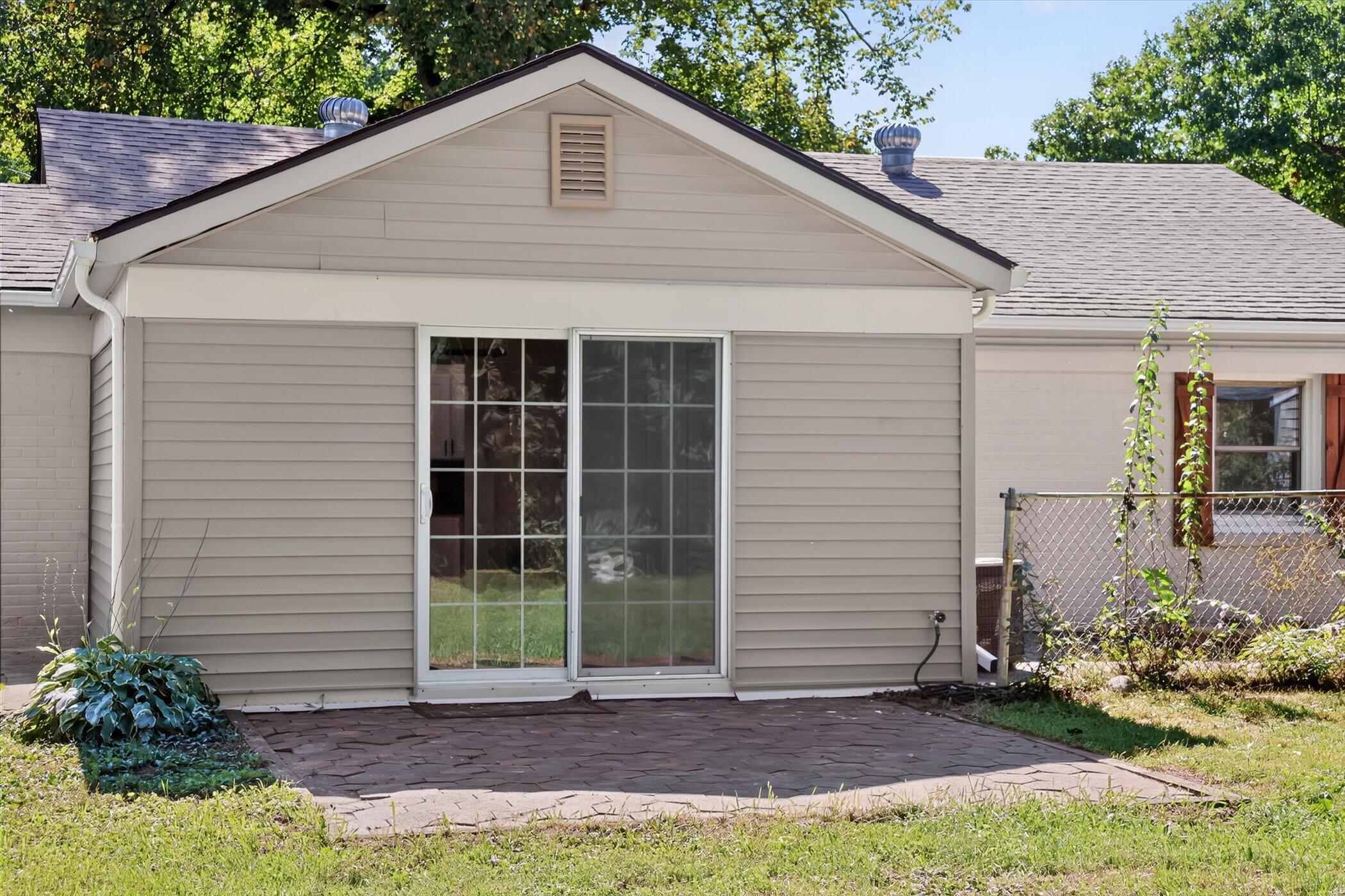 Rear of a single-story home with a sliding glass door, paved patio, and fenced garden.
