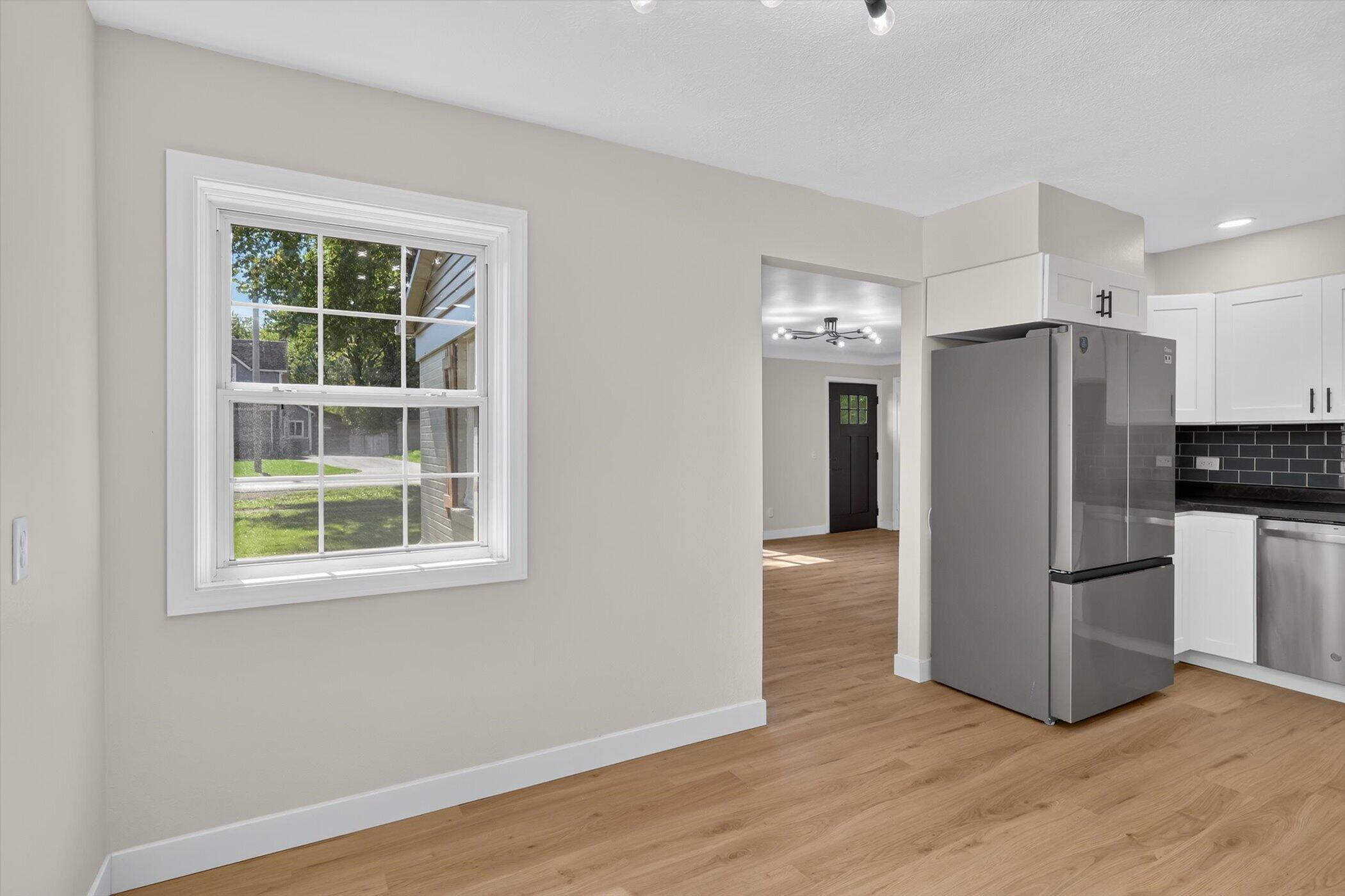 Kitchen with white cabinets, stainless steel appliances, black tile backsplash, and a large window.