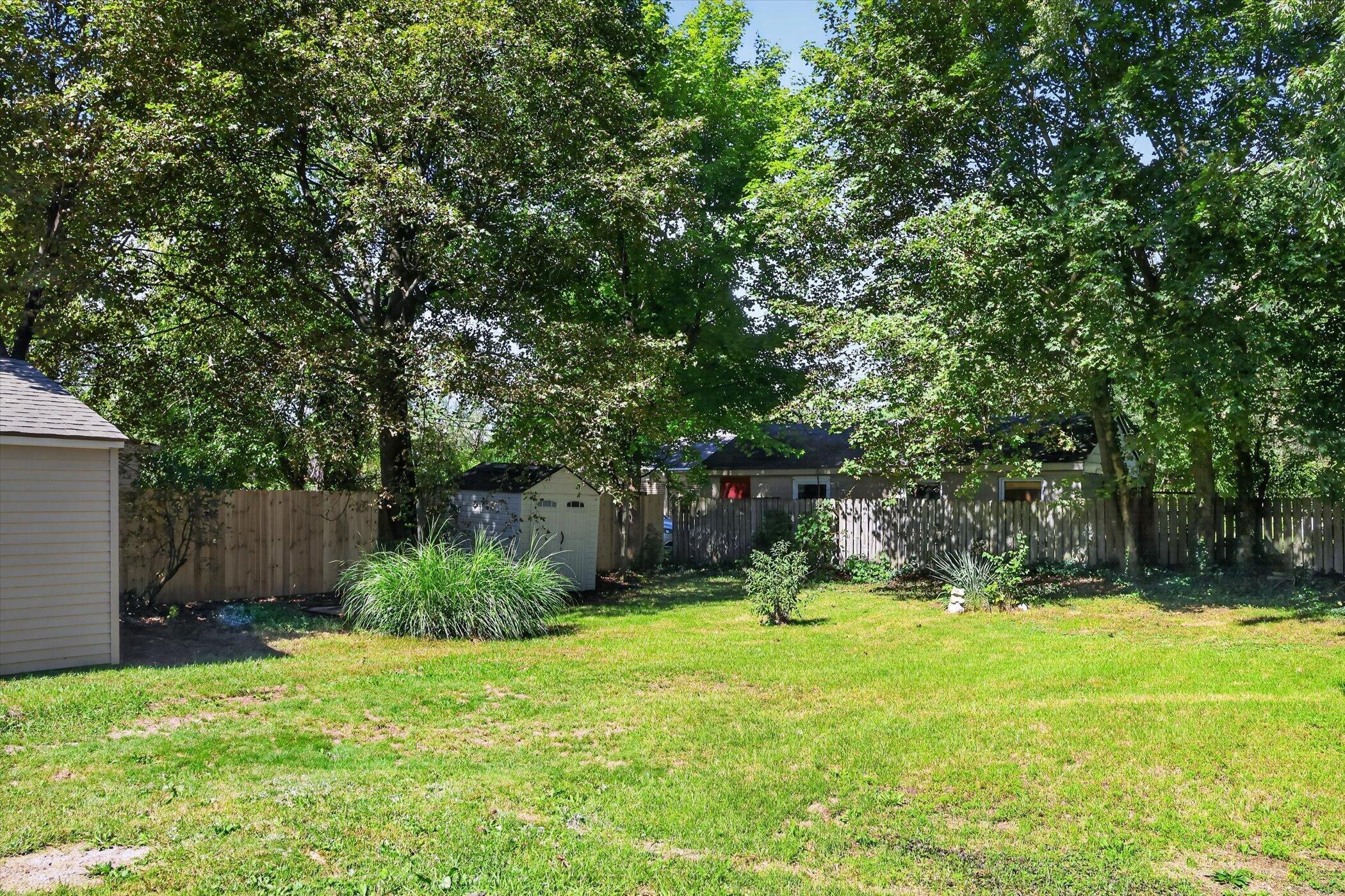Backyard with a broad lawn, mature trees, wooden fencing, and a small shed.