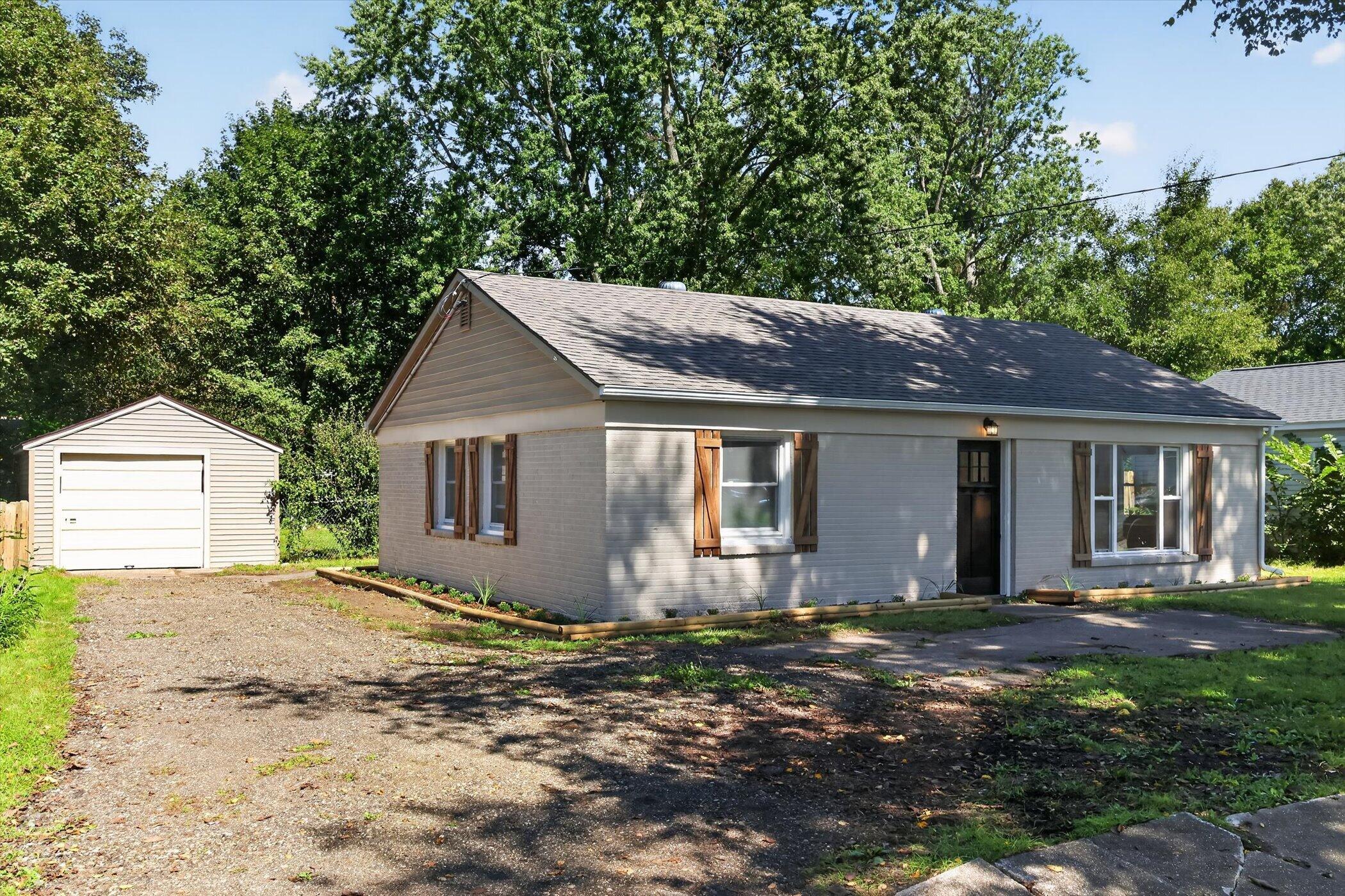 Single-story gray house with wood shutters, a detached garage, and a gravel driveway.