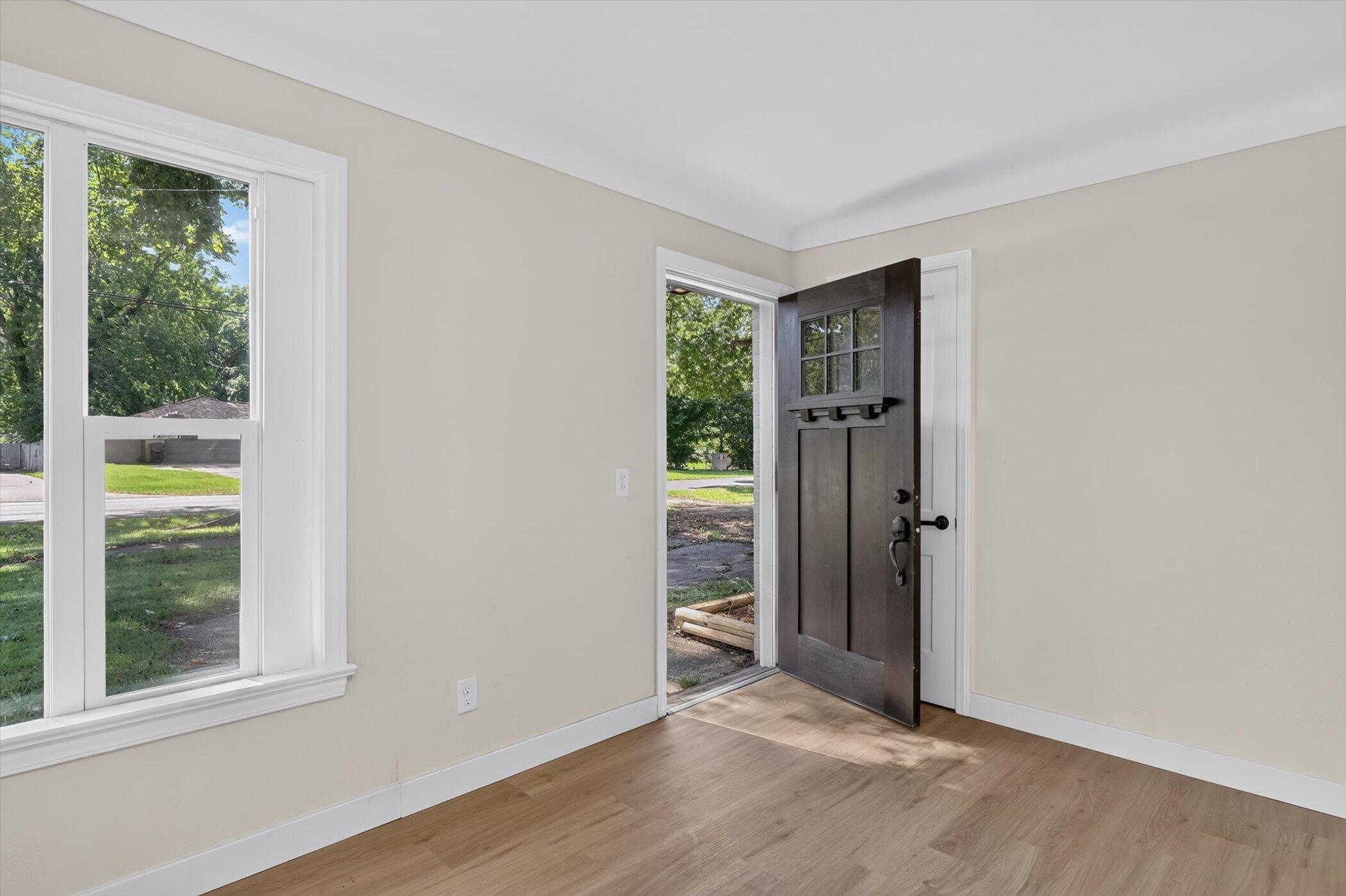 Vacant entryway with light wood floors, a large window, and an open dark front door.