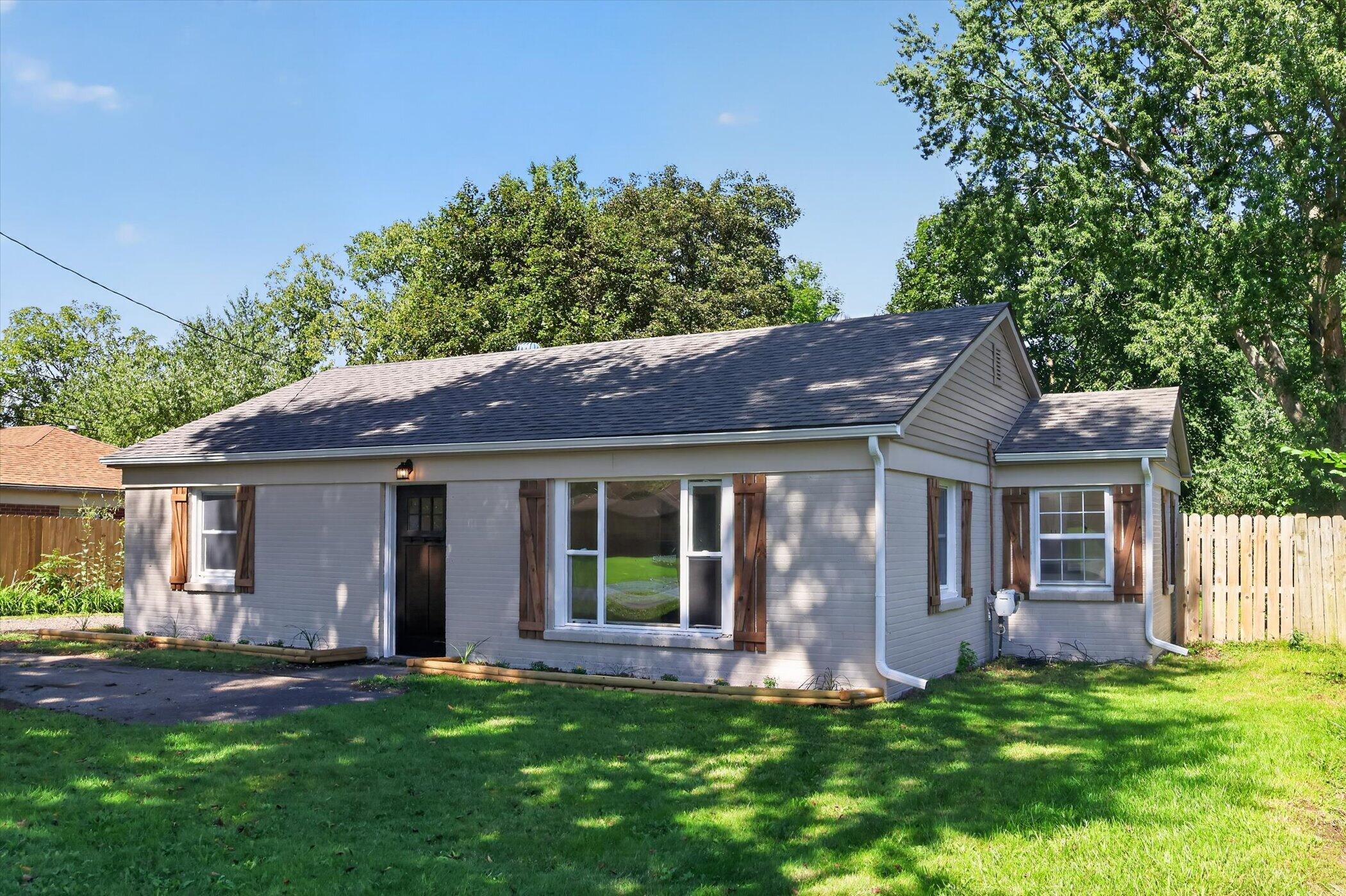Single-story gray house with wooden shutters and a shaded front lawn.