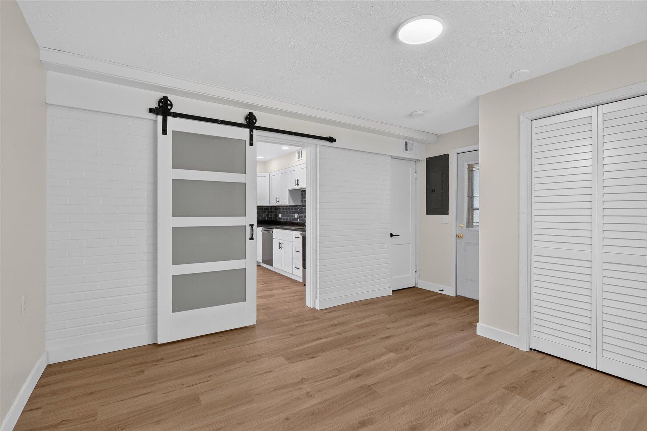 Empty room with wood-look flooring, a sliding barn-style door, and a kitchen visible through the doorway.