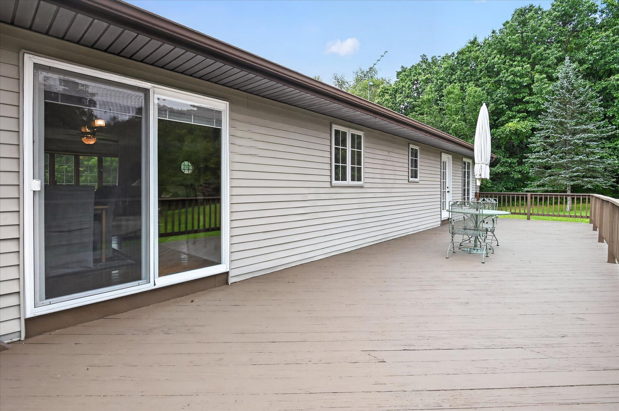 Spacious wooden deck beside a gray-sided home, with sliding doors and outdoor dining furniture.