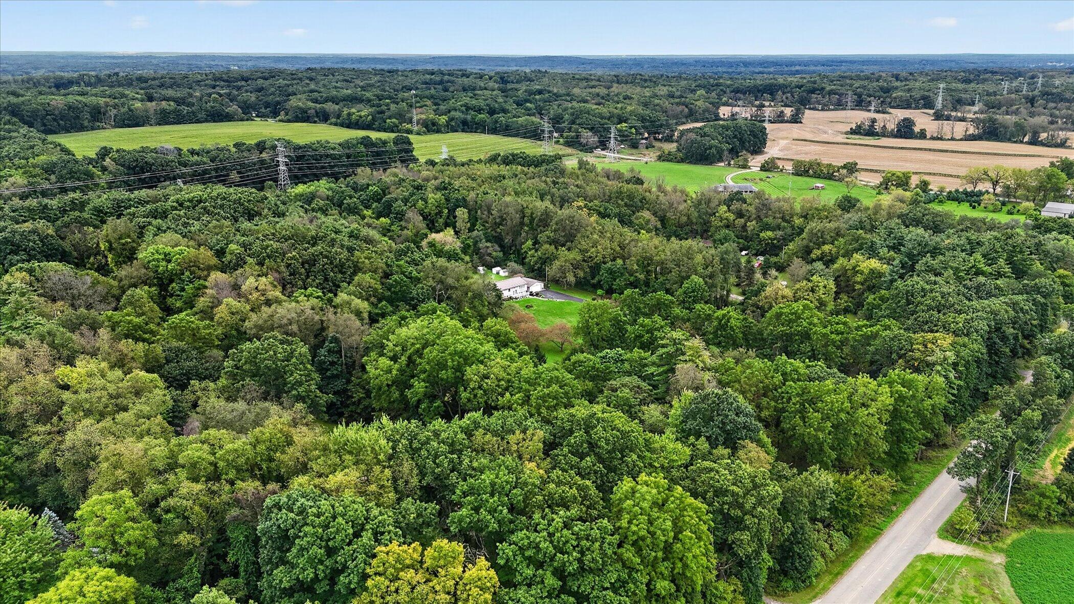 Aerial view of a wooded rural property, with a house, open fields, and transmission lines.