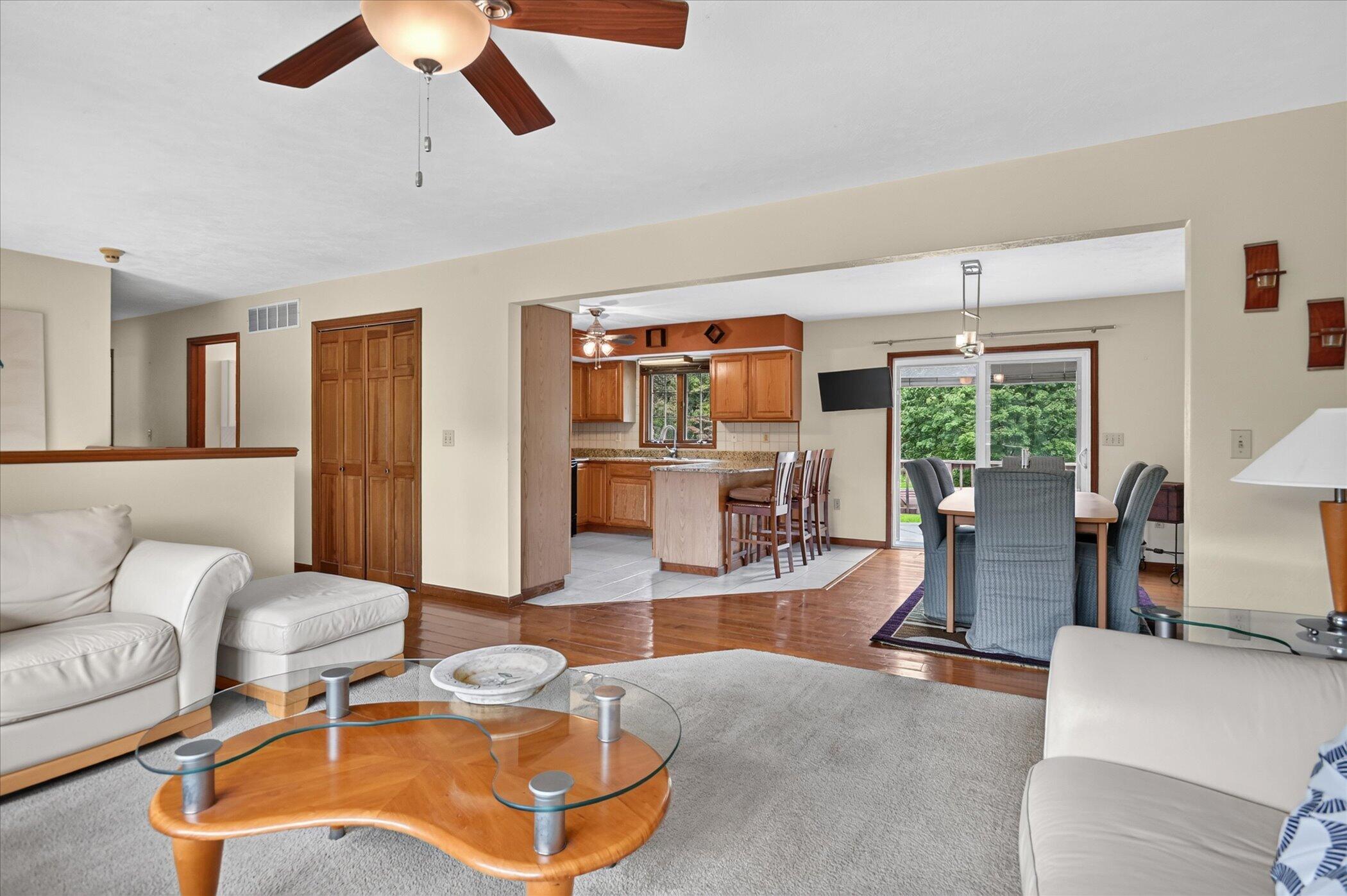 Open-plan living room and kitchen with wood cabinetry, a dining area, and sliding glass doors to greenery.
