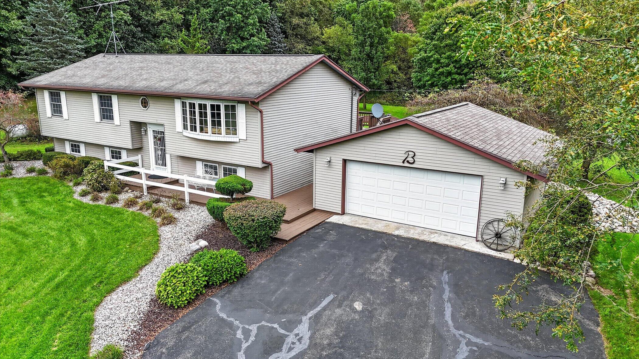 Gray split-level home with burgundy trim, attached garage, landscaped lawn, and mature trees.