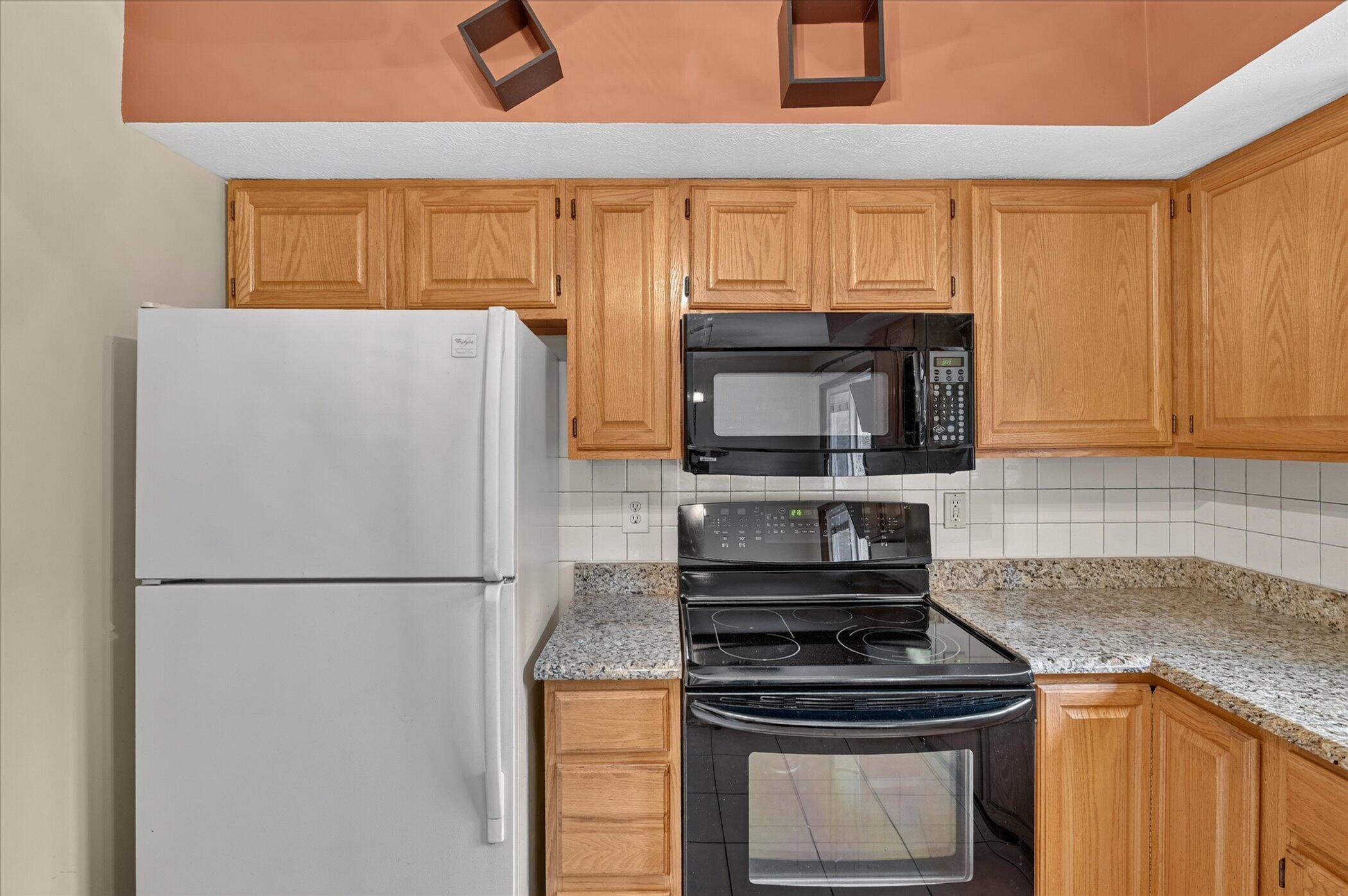 Kitchen with wood cabinets, speckled countertops, and black range beside a white refrigerator.