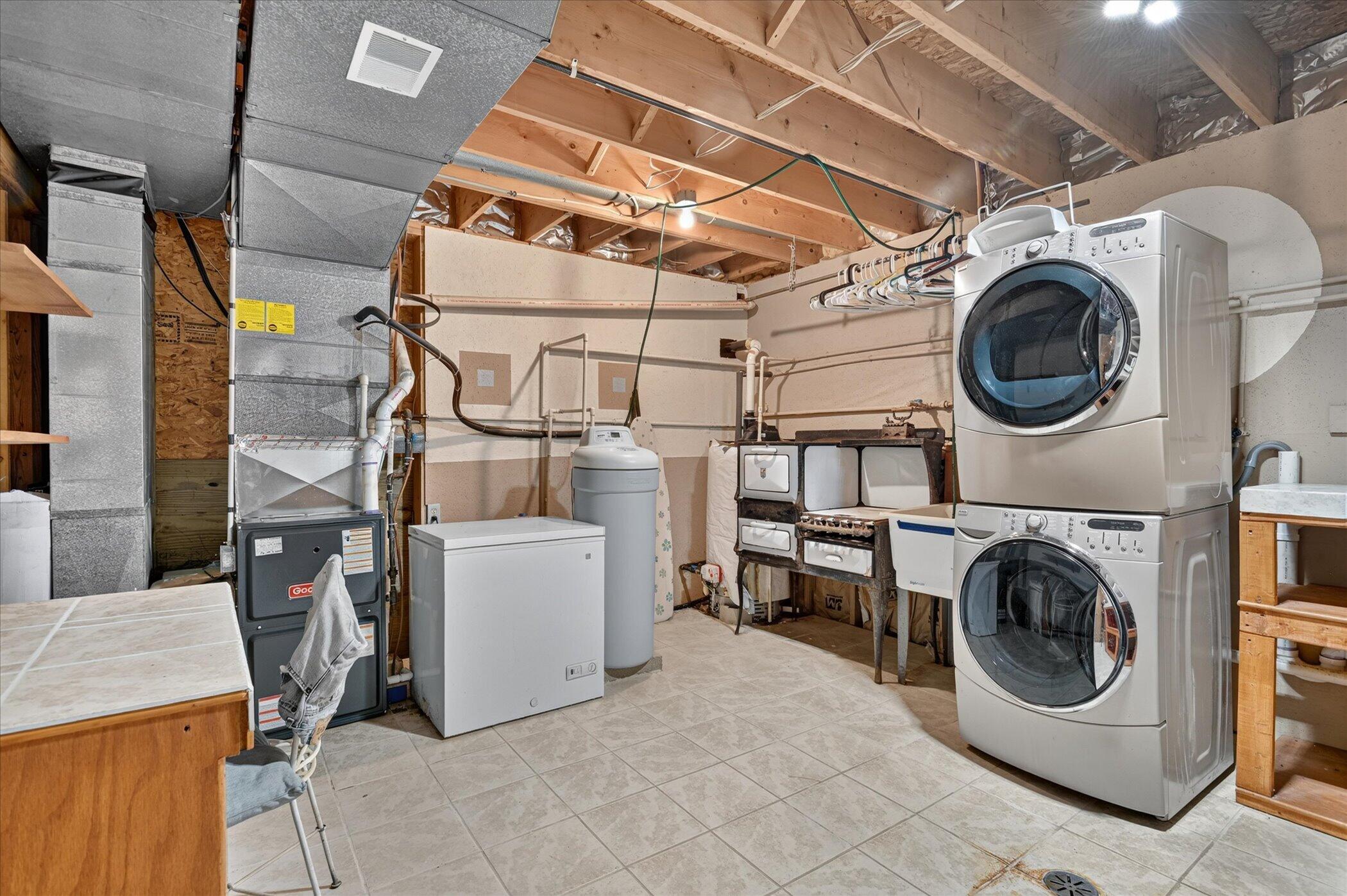 Basement laundry room with stacked washer and dryer, chest freezer, and exposed ceiling joists.