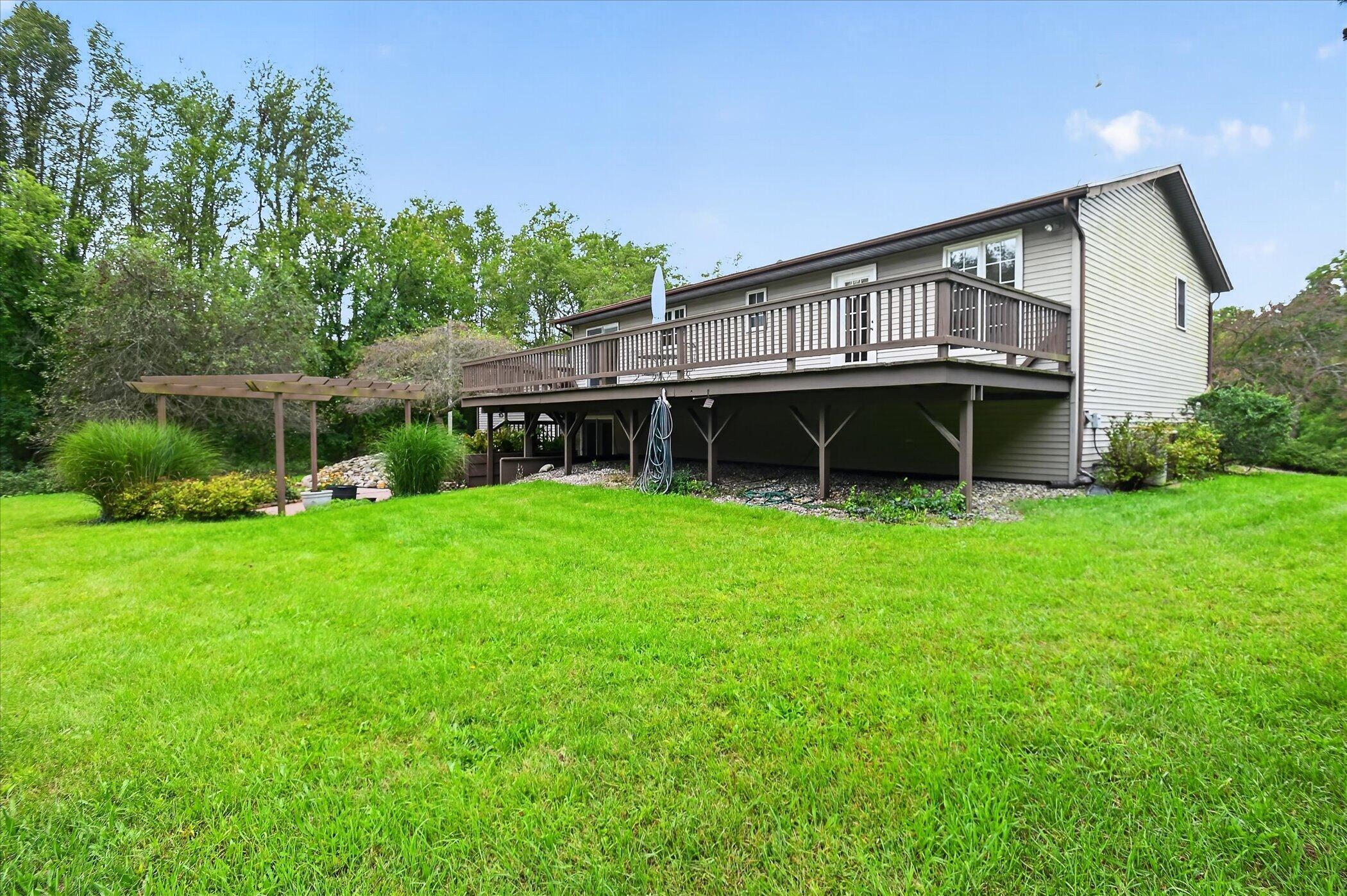 House rear with a large elevated deck, pergola, and broad lawn.