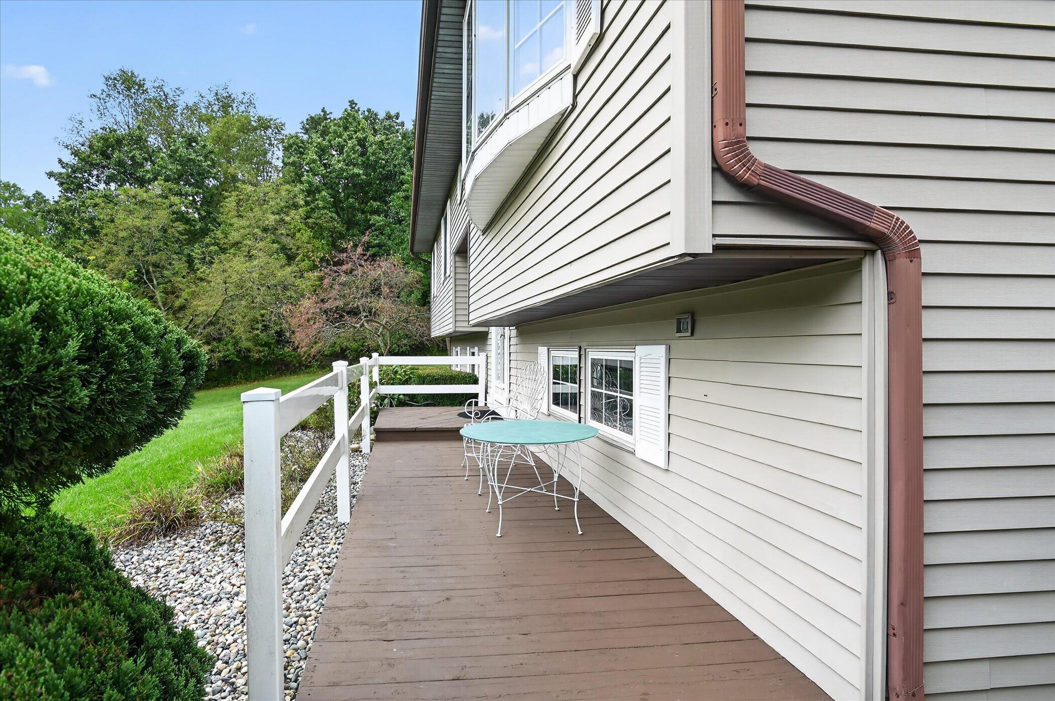 Wooden deck beside a light-sided house, furnished with a patio table and chairs and bordered by a white railing.