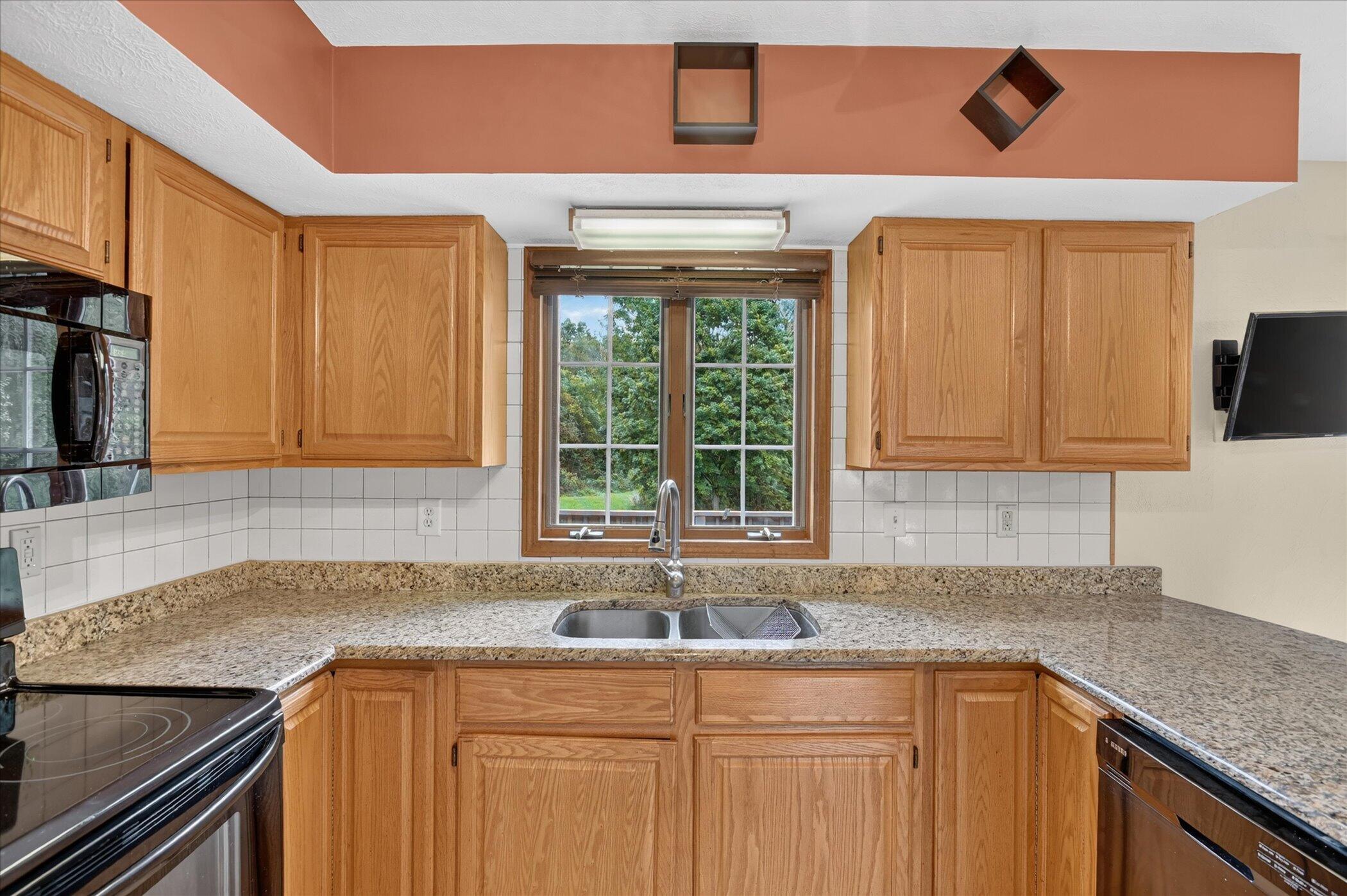 Kitchen with honey-colored cabinets, granite counters, and a double sink beneath a window.