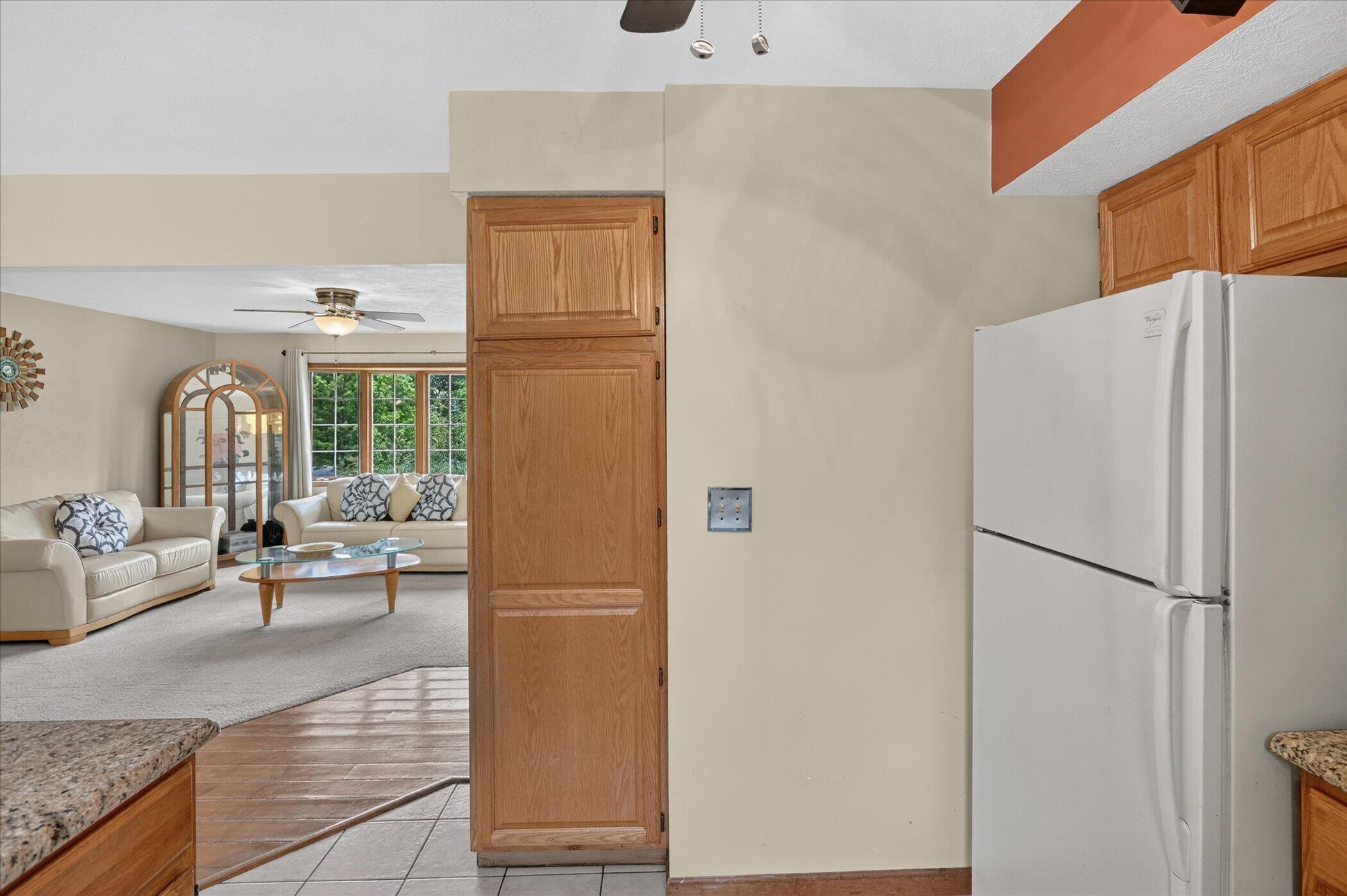 Kitchen with oak cabinets and white refrigerator, opening onto a living room with cream sofas.