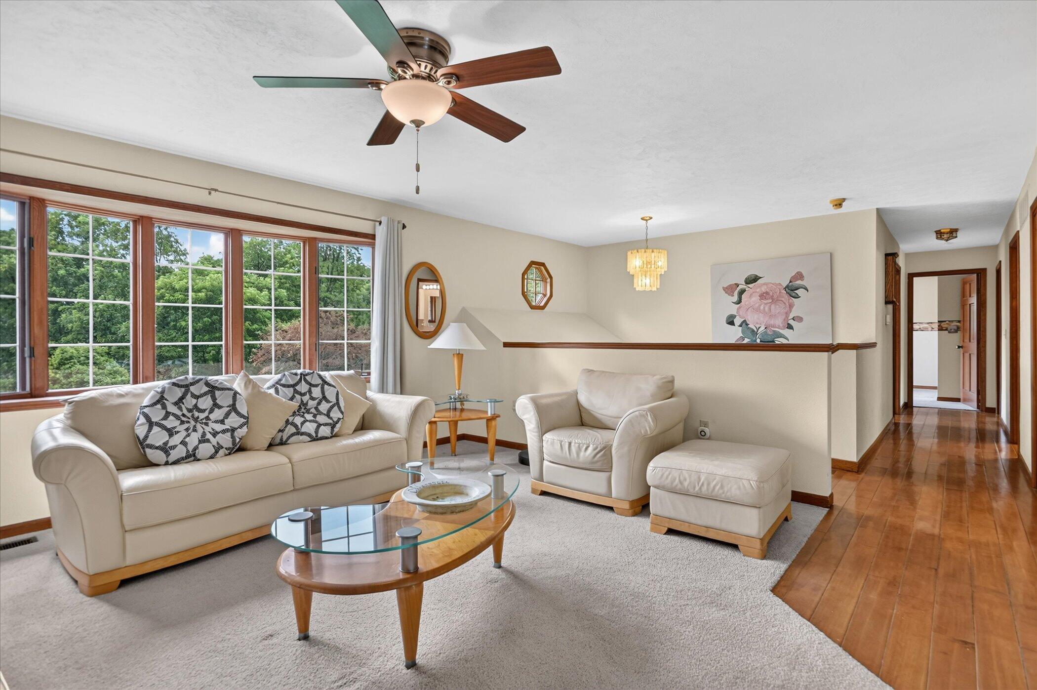 Living room with cream seating, large wood-trimmed windows, and a polished hardwood hallway.