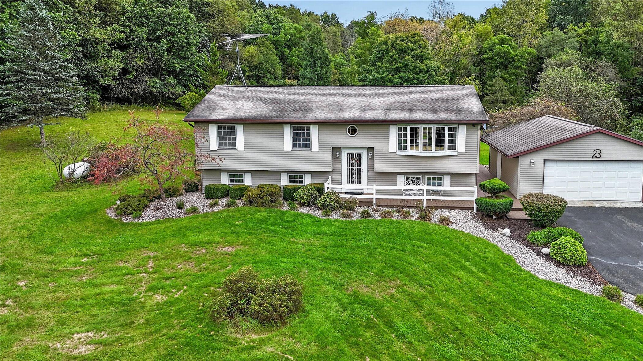 Gray split-level house and detached garage surrounded by a broad green lawn and mature trees.
