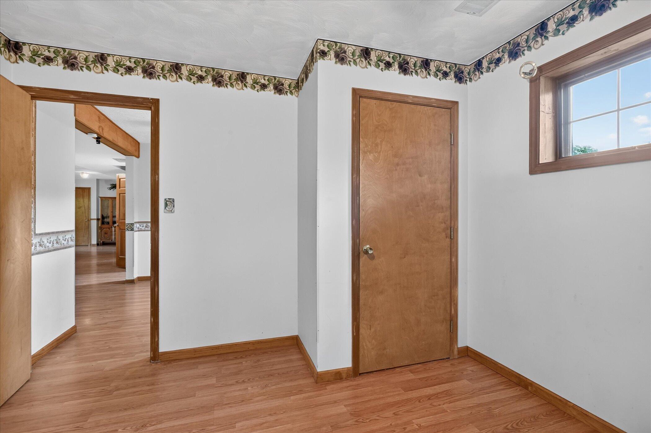 Empty room with wood-look flooring, floral wall borders, a wooden door, and a window.