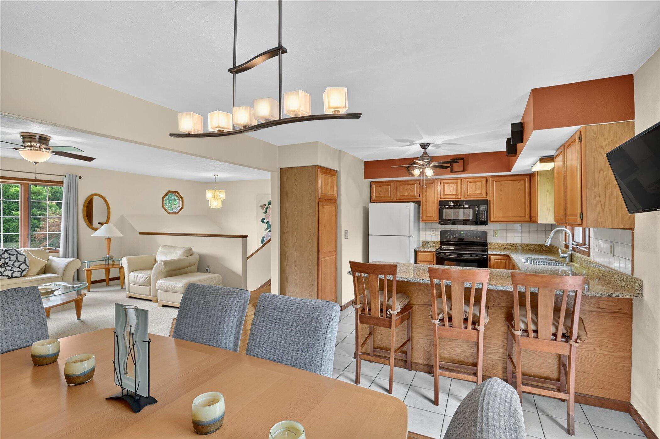 Open-plan kitchen and living area with wood cabinets, granite breakfast bar, and large windows.