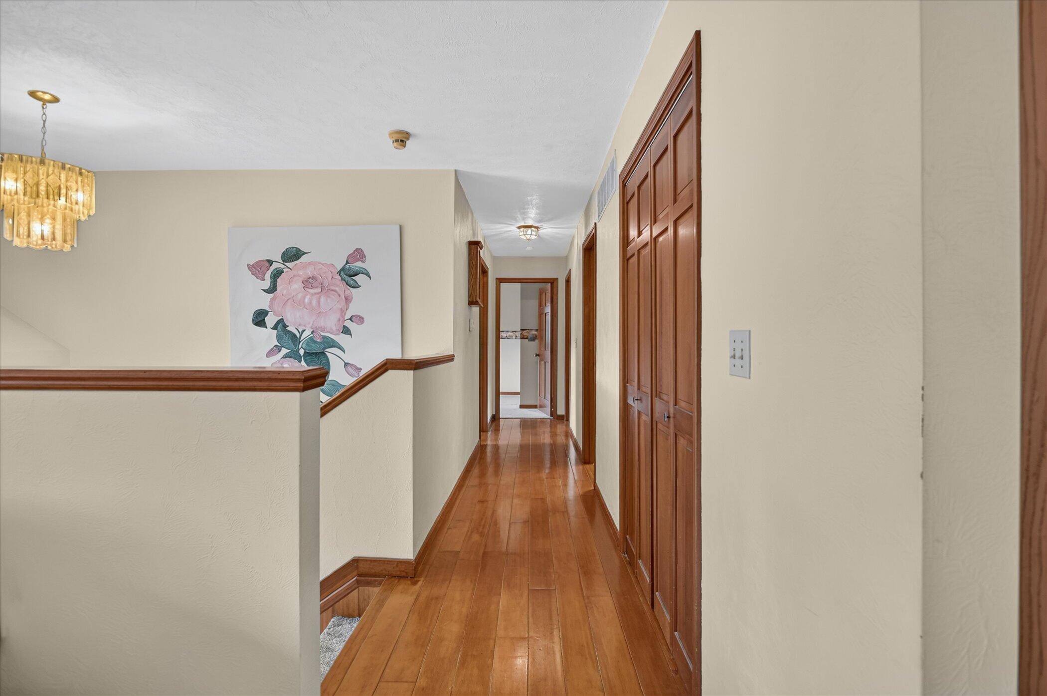 Hallway with polished wood floors, paneled doors, and a large floral painting beside the stairs.