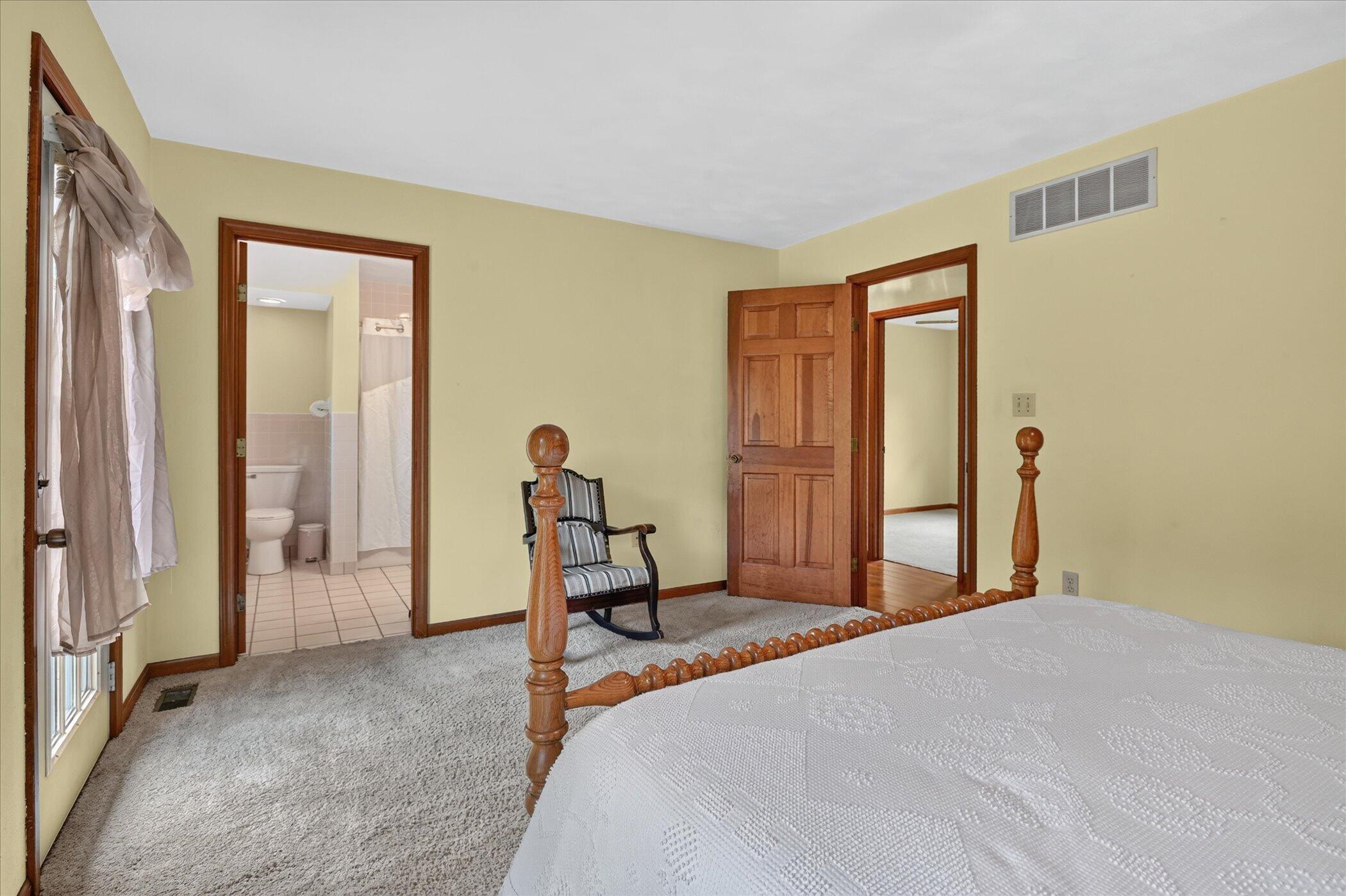 Bedroom with a wooden bed and rocking chair, opening to an adjoining bathroom.