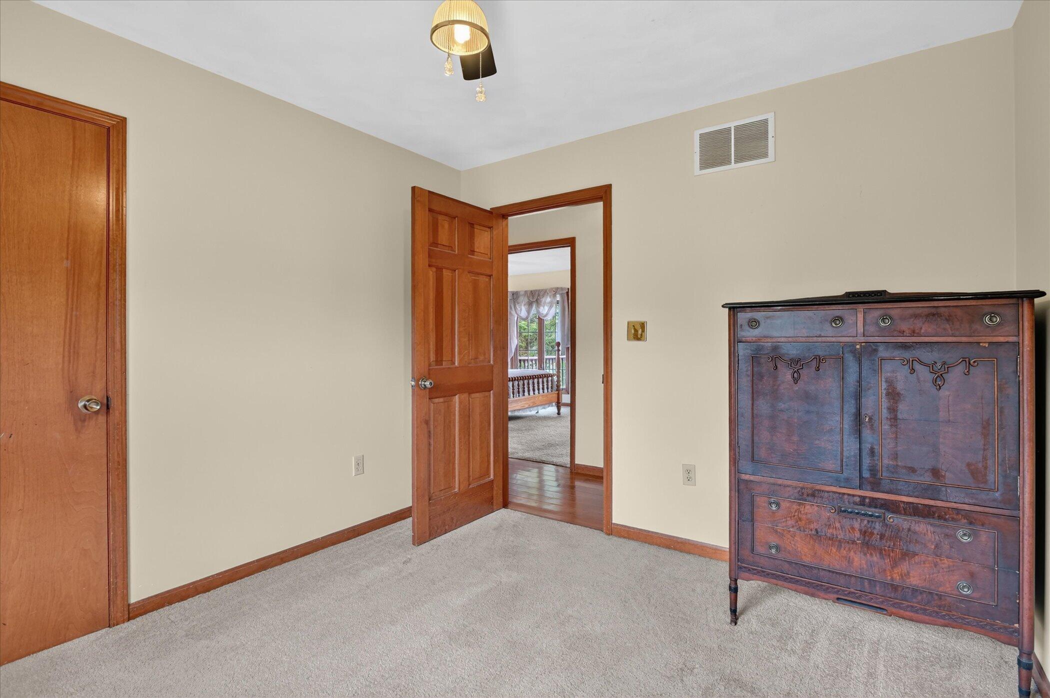 Carpeted bedroom with a dark wooden dresser and an open doorway to another room.