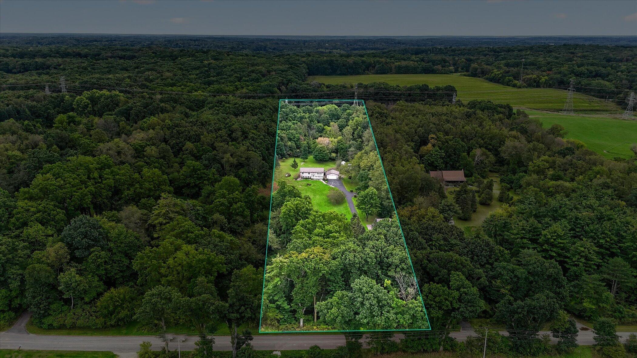 Aerial view of a wooded property outlined in teal, with a house, driveway, and road frontage.