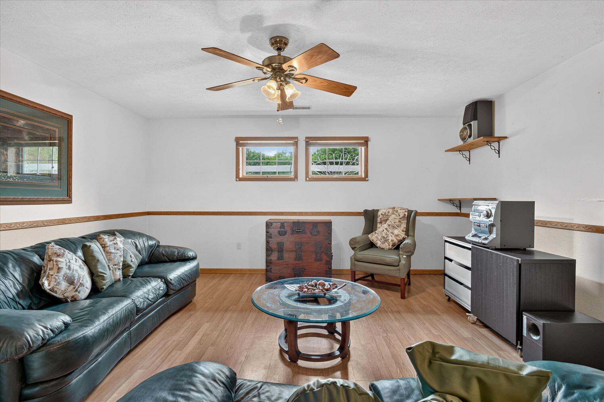 Living room with dark leather sofa, glass coffee table, wood flooring, and two small windows.