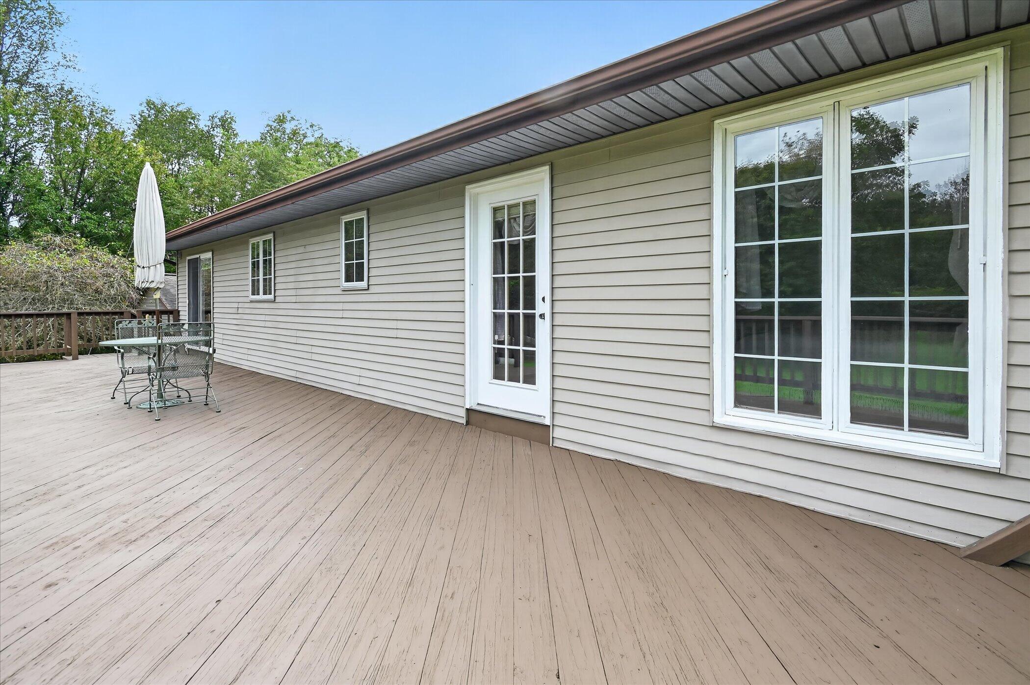 Spacious wood deck beside a light-sided home, with patio seating and large white-framed windows.